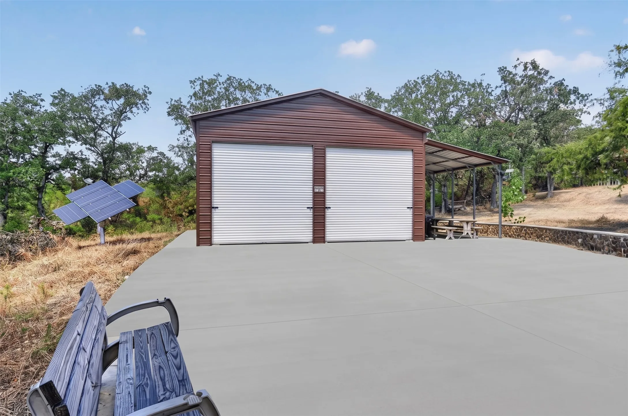 Two-bay metal garage with roll-up doors, an attached covered patio, and concrete paving