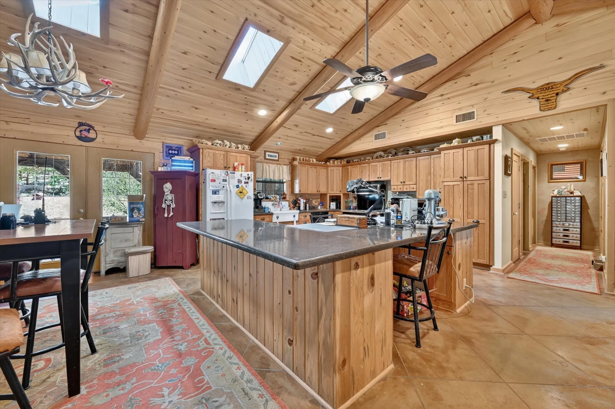Kitchen featuring a vaulted wood-paneled ceiling, exposed wood beams, skylights, wood cabinetry, and a substantial island with a dark countertop