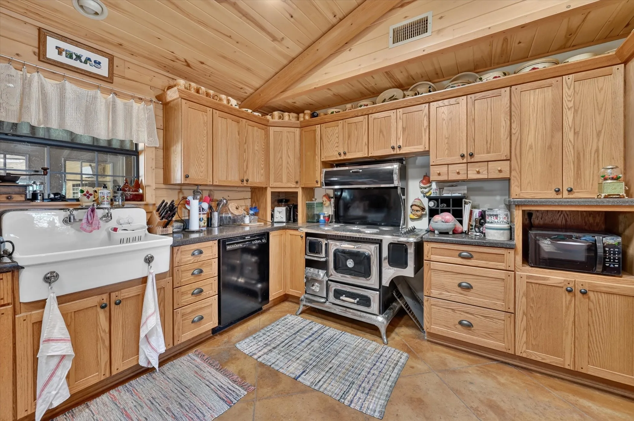Wood-paneled ceilings, extensive wood cabinetry, farmhouse sink, black dishwasher, and built-in microwave
