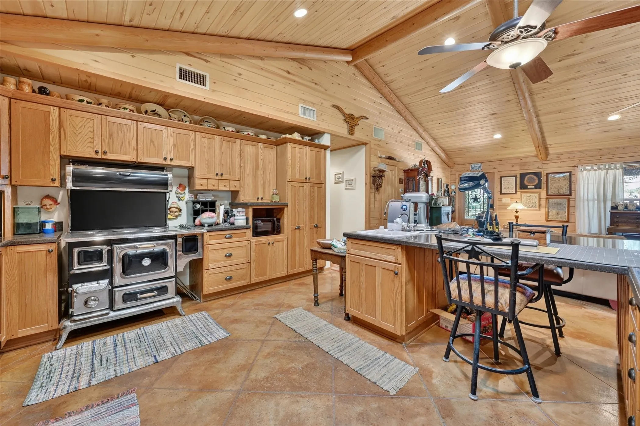 Vaulted wood-paneled ceiling with exposed beams, wood-finish cabinetry, built-in range, and a kitchen island with seating