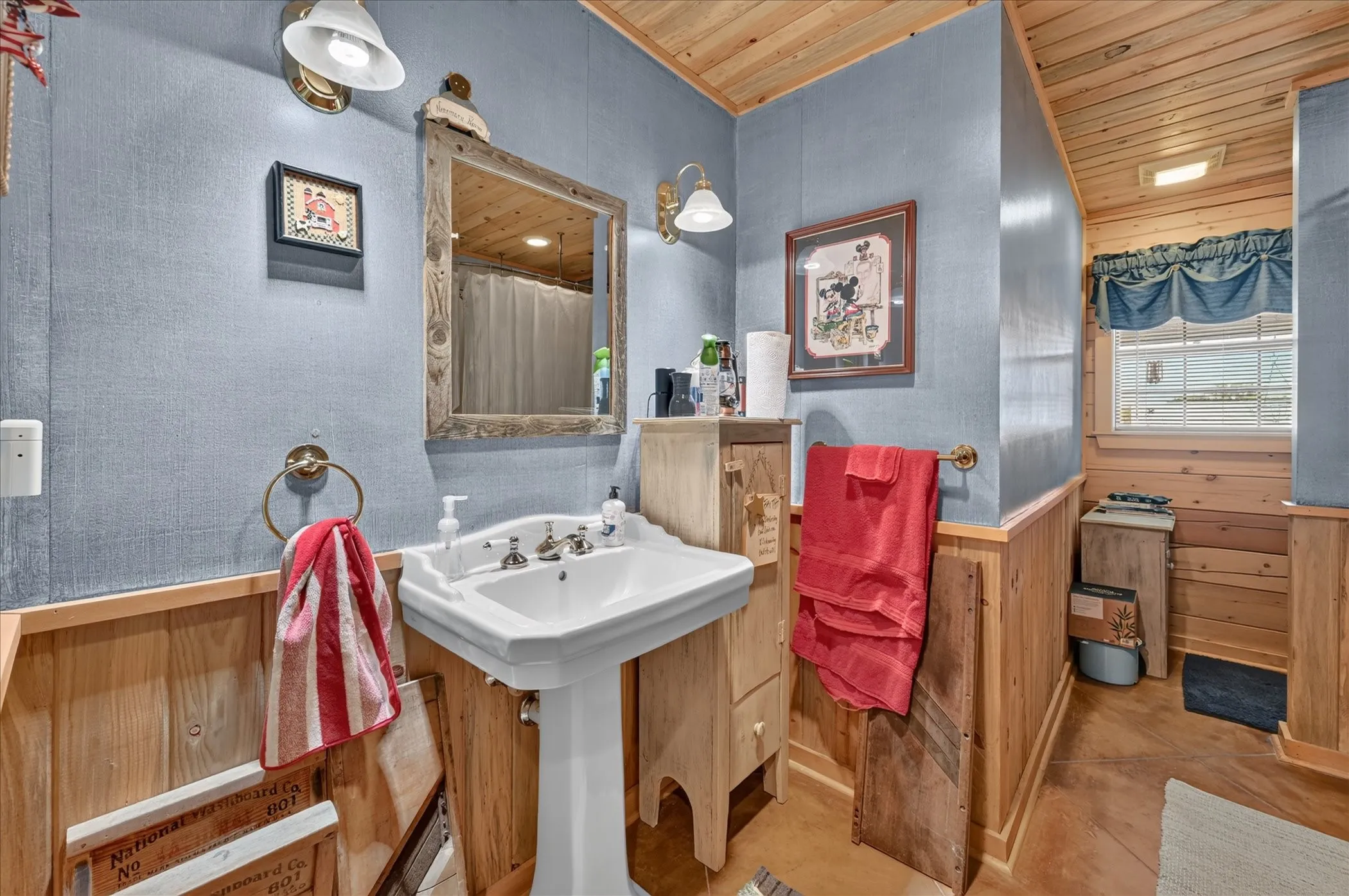 Pedestal sink with polished chrome fixtures, wood-paneled walls, and a wood-slat ceiling