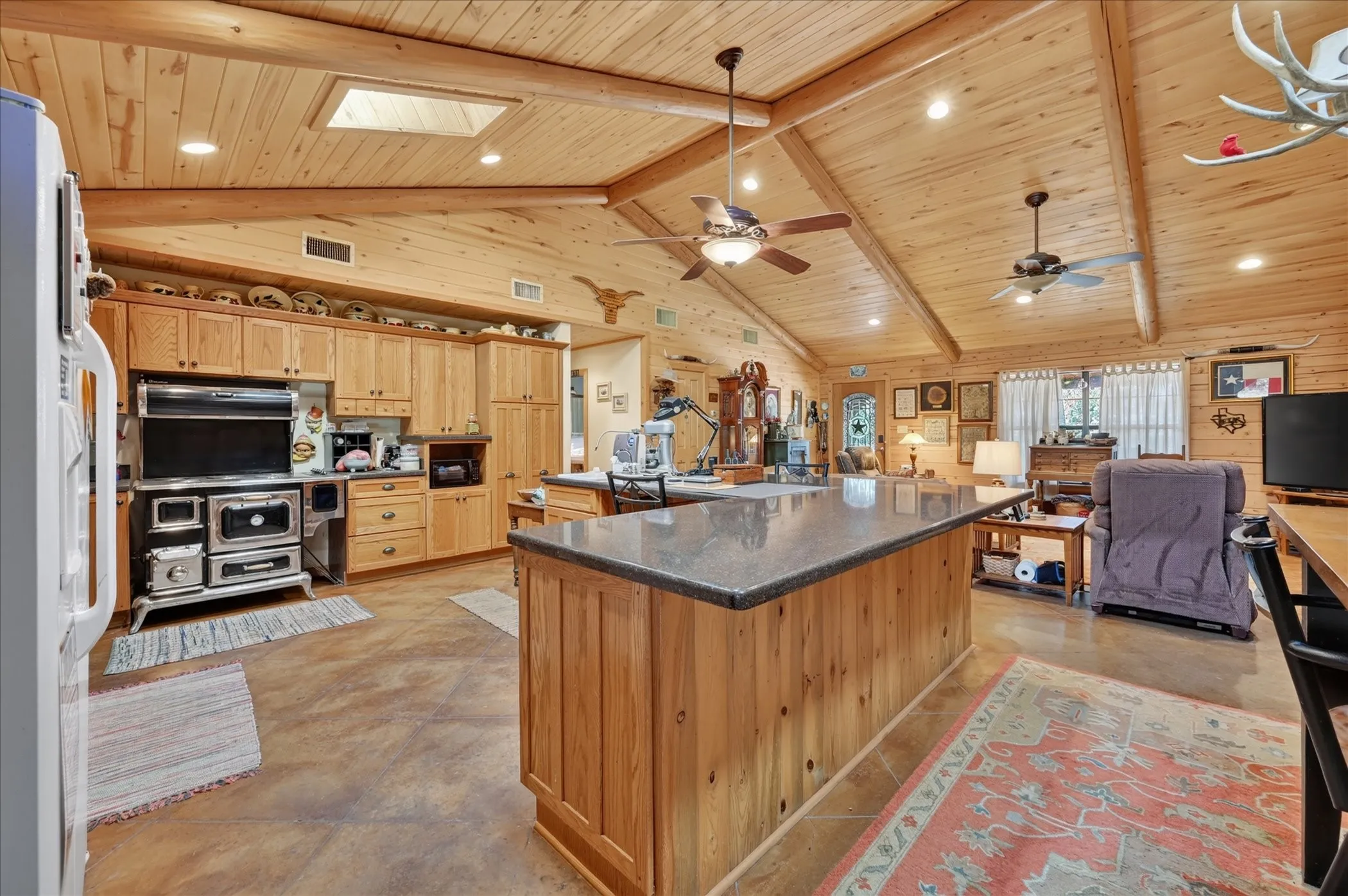 Expansive open-concept room featuring vaulted wood-paneled ceilings, exposed wood beams, a skylight, recessed lighting, and ceiling fans