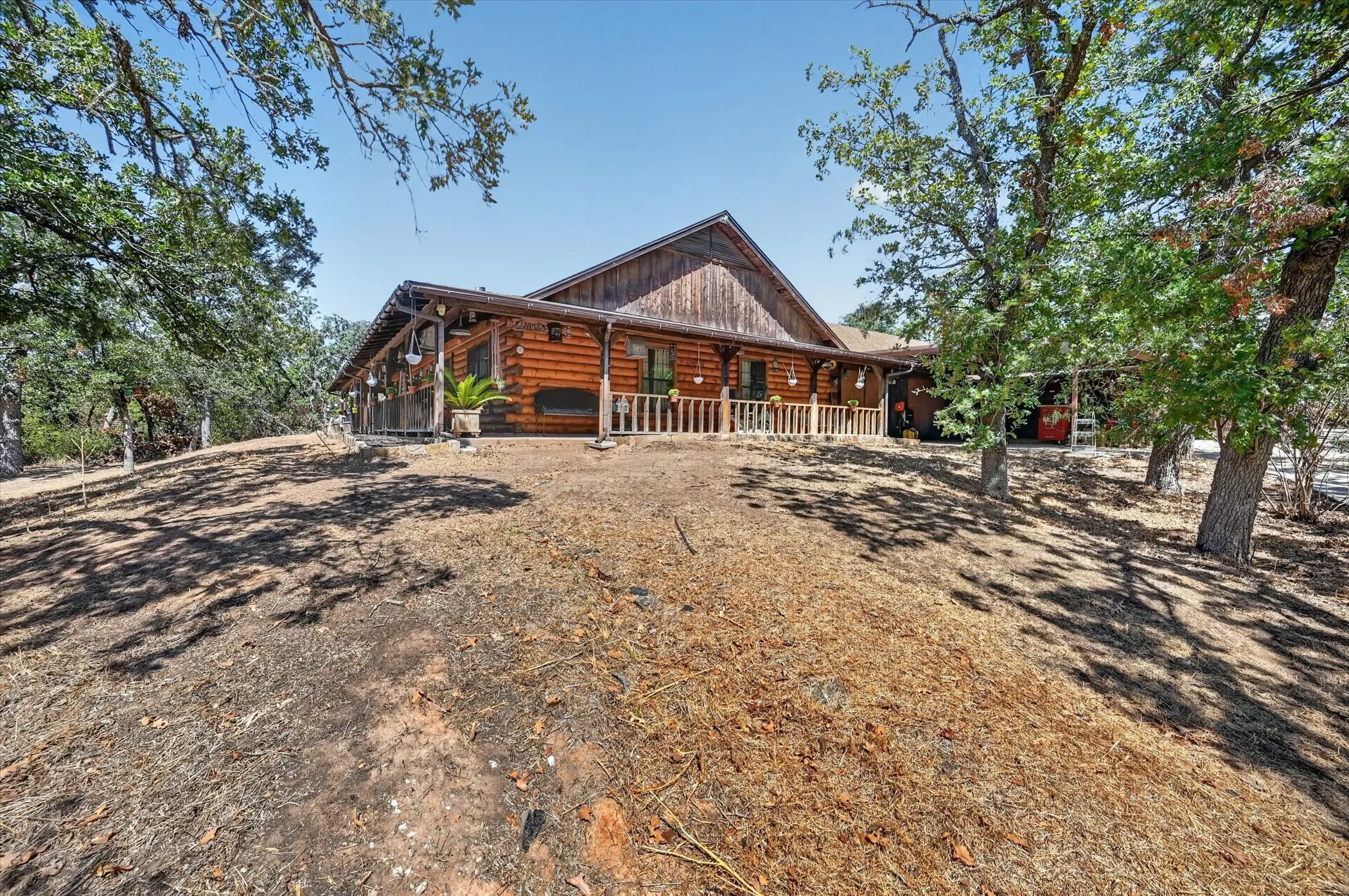 Log cabin exterior with an expansive covered front porch, gabled roofline, and mature trees
