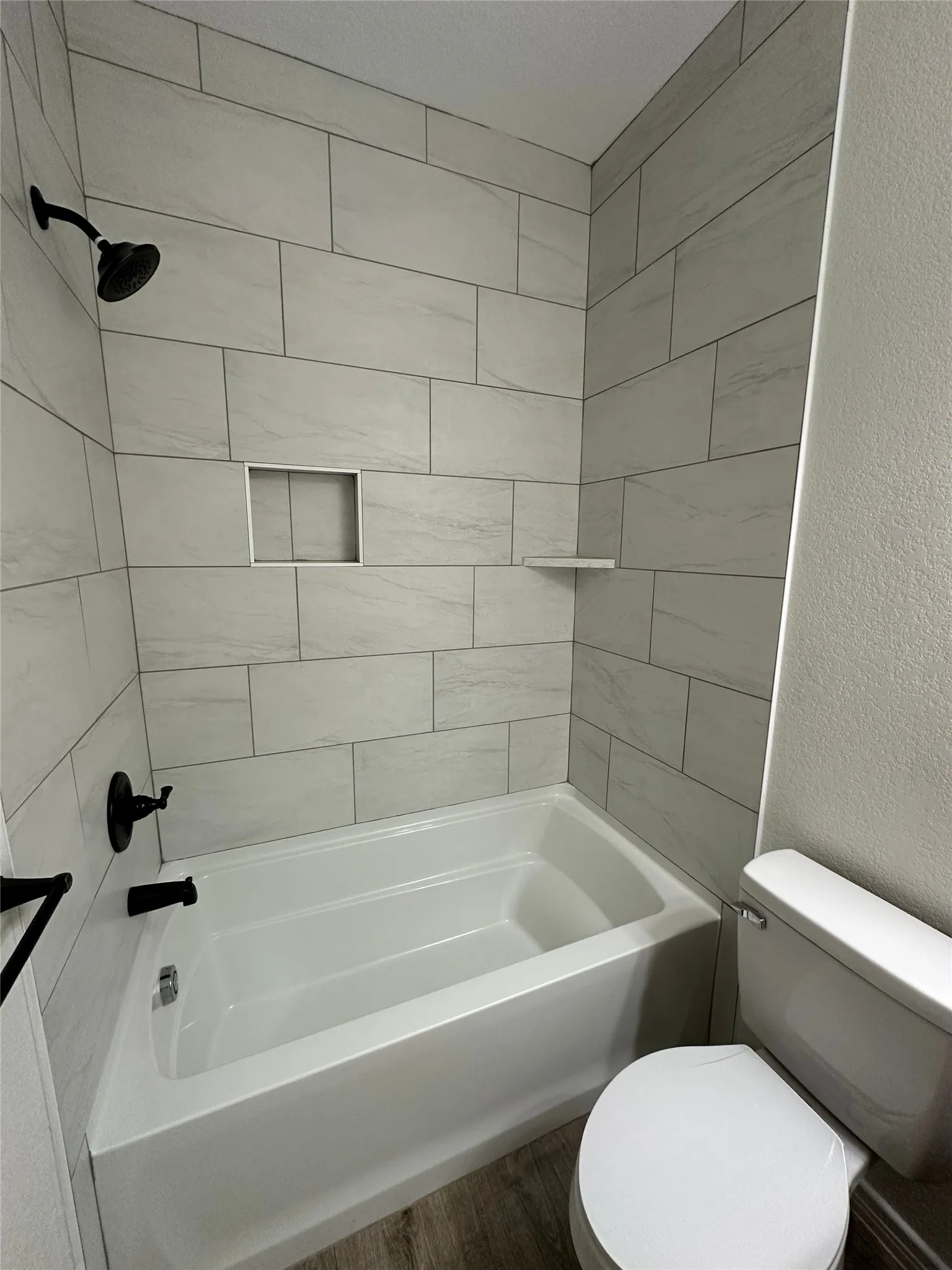Bathtub with matte black fixtures, tiled surround with a recessed niche, and a built-in shelf