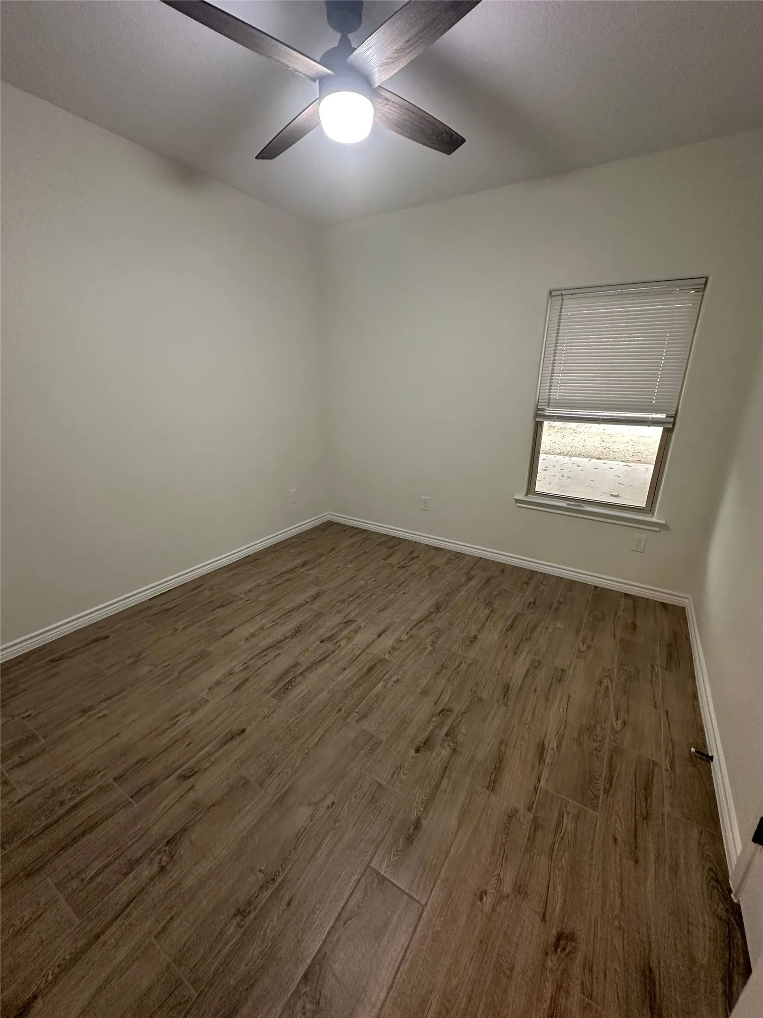 Wood-finish plank flooring, ceiling fan with integrated lighting, and a window featuring horizontal blinds