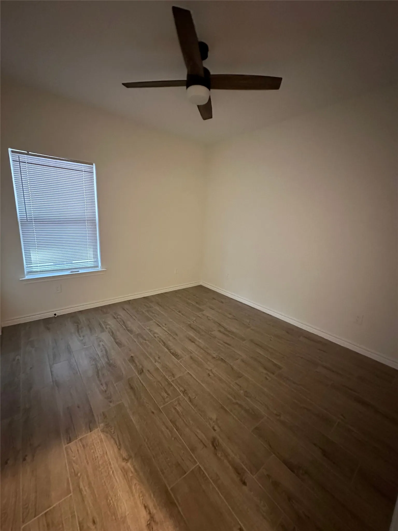 Wood-finish tile flooring throughout, featuring a ceiling fan with integrated lighting and a window with blinds