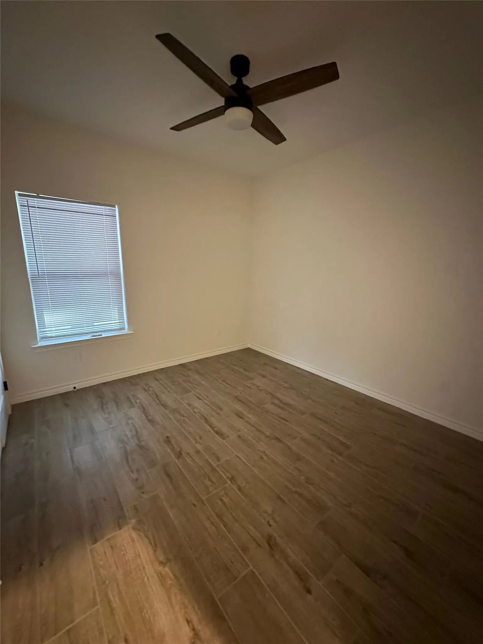 Wood-finish flooring, ceiling fan with integrated lighting, and a window with blinds