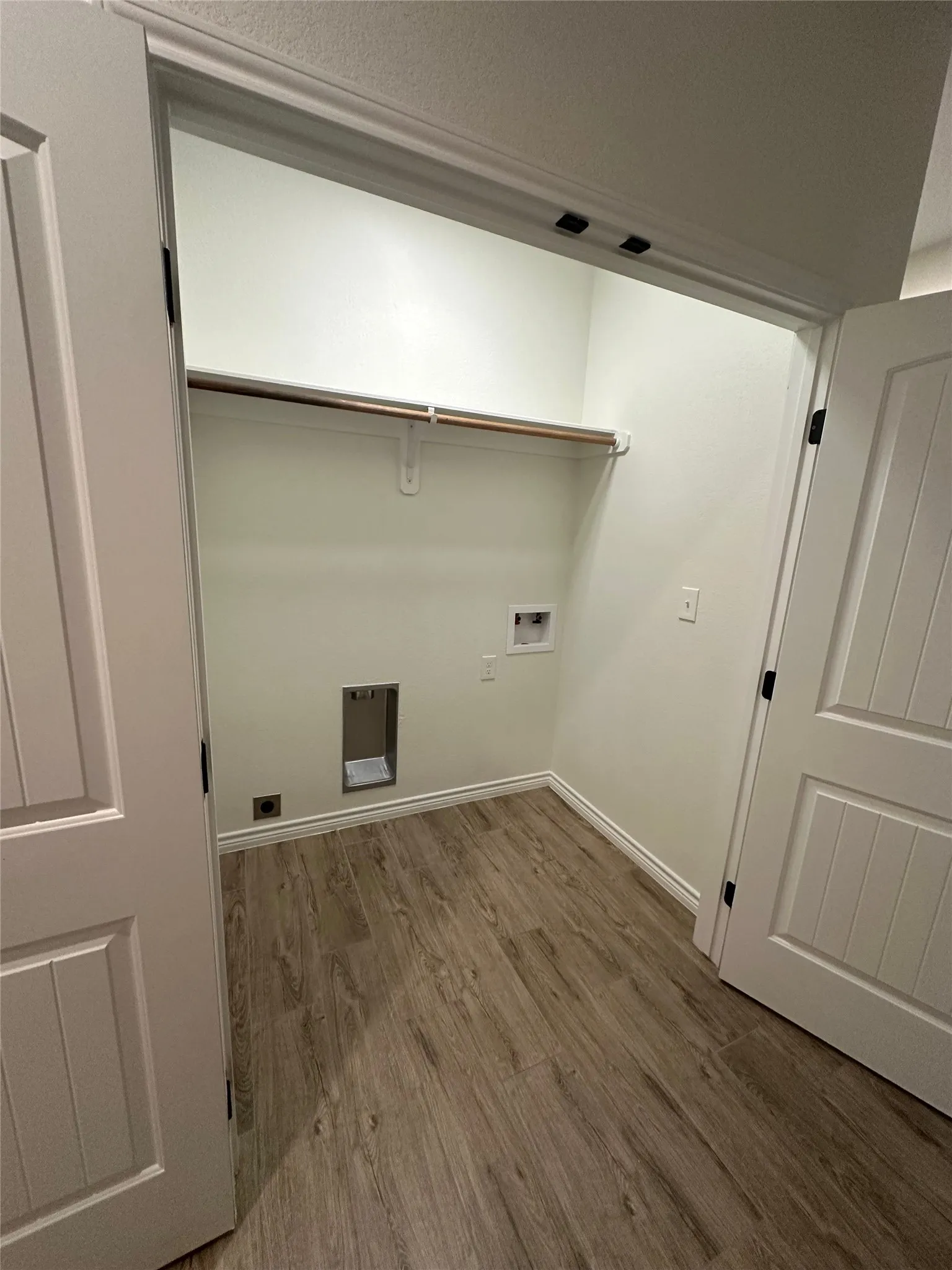 Dedicated laundry space featuring wood-finish flooring, a built-in hanging rod, and white panel doors