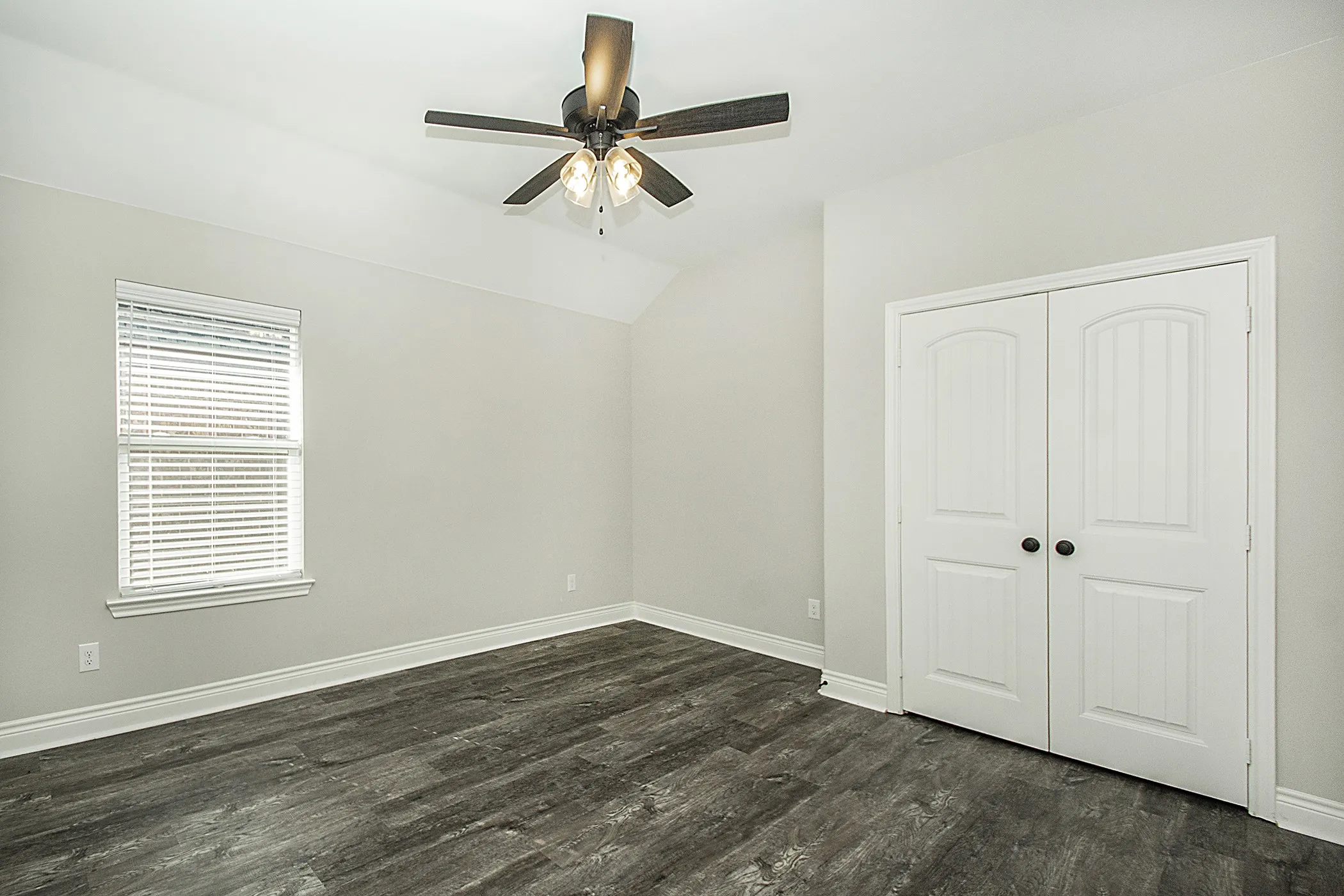 Vaulted ceiling with a ceiling fan, window with blinds, wood-finish flooring, and double closet doors