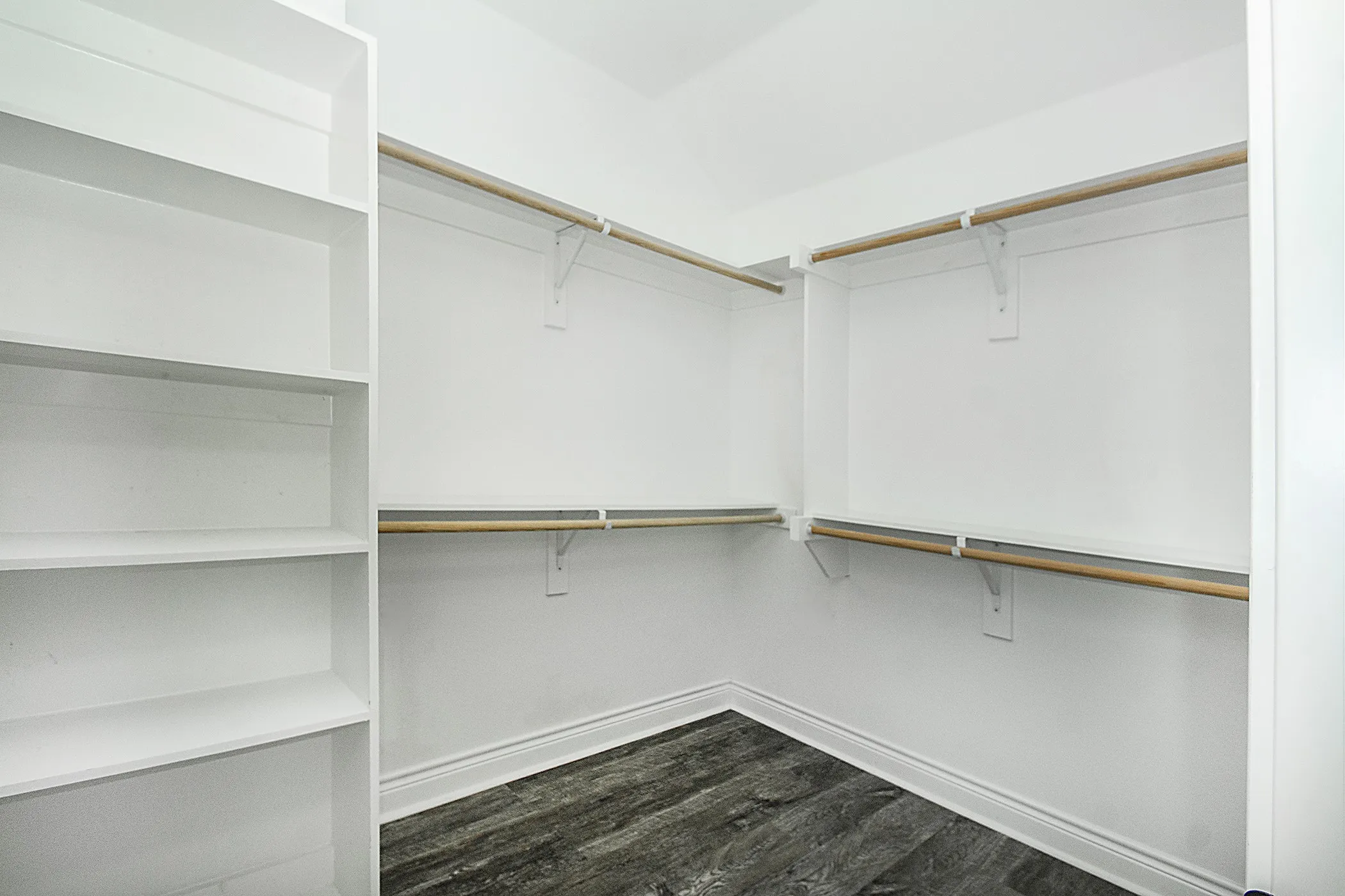 Custom closet featuring built-in shelving, multiple hanging rods, and wood-finish flooring