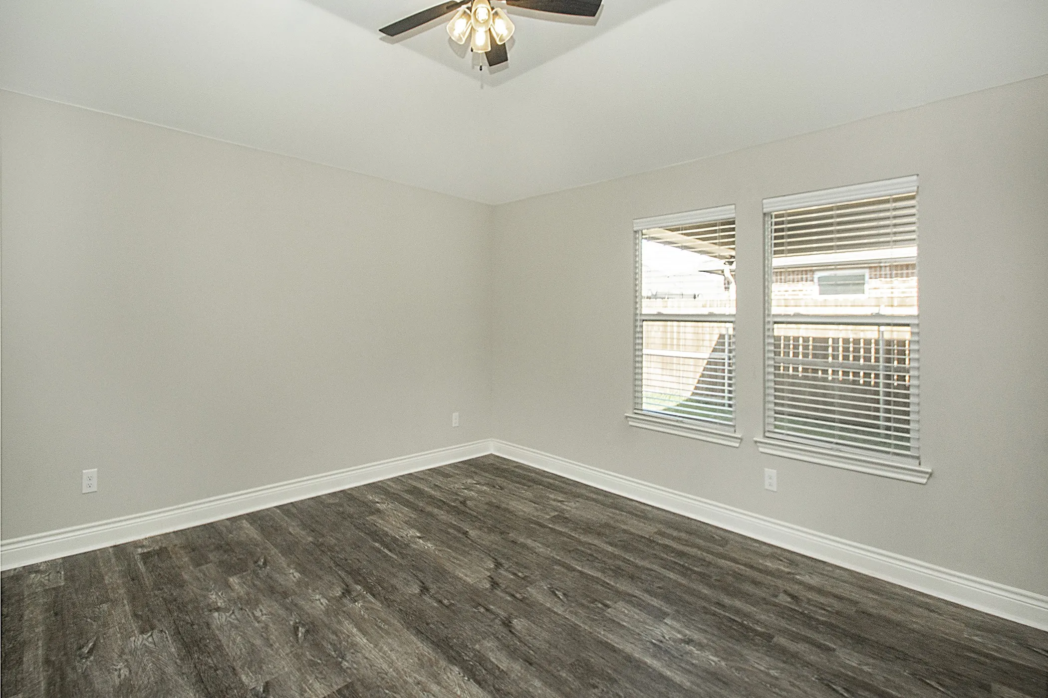 Wood-finish flooring, neutral wall tones, two windows with blinds, and ceiling fan with integrated lighting