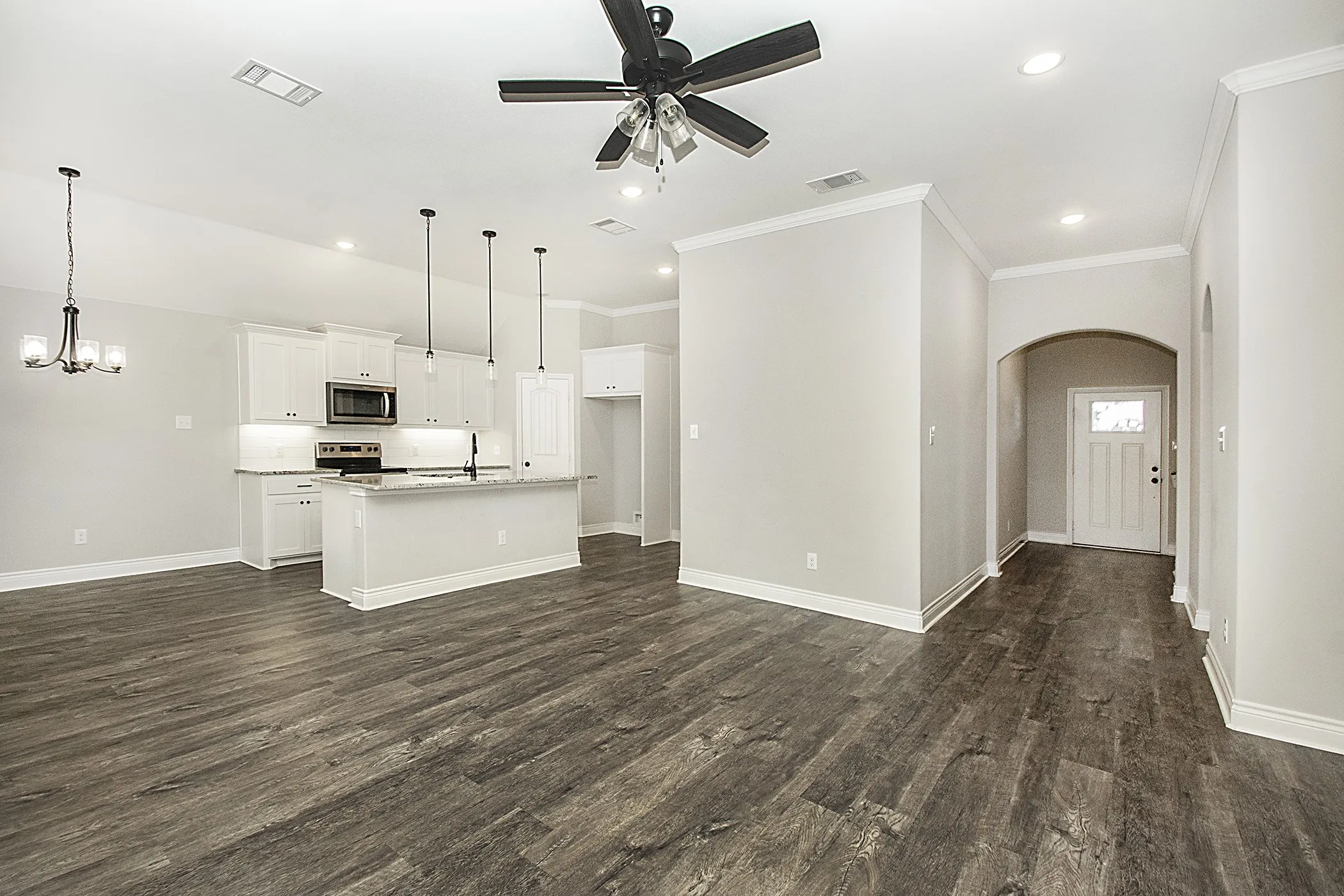 Open-concept living area featuring wood-finish flooring, a contemporary kitchen with white cabinetry and a central island, recessed lighting, and an arched entry
