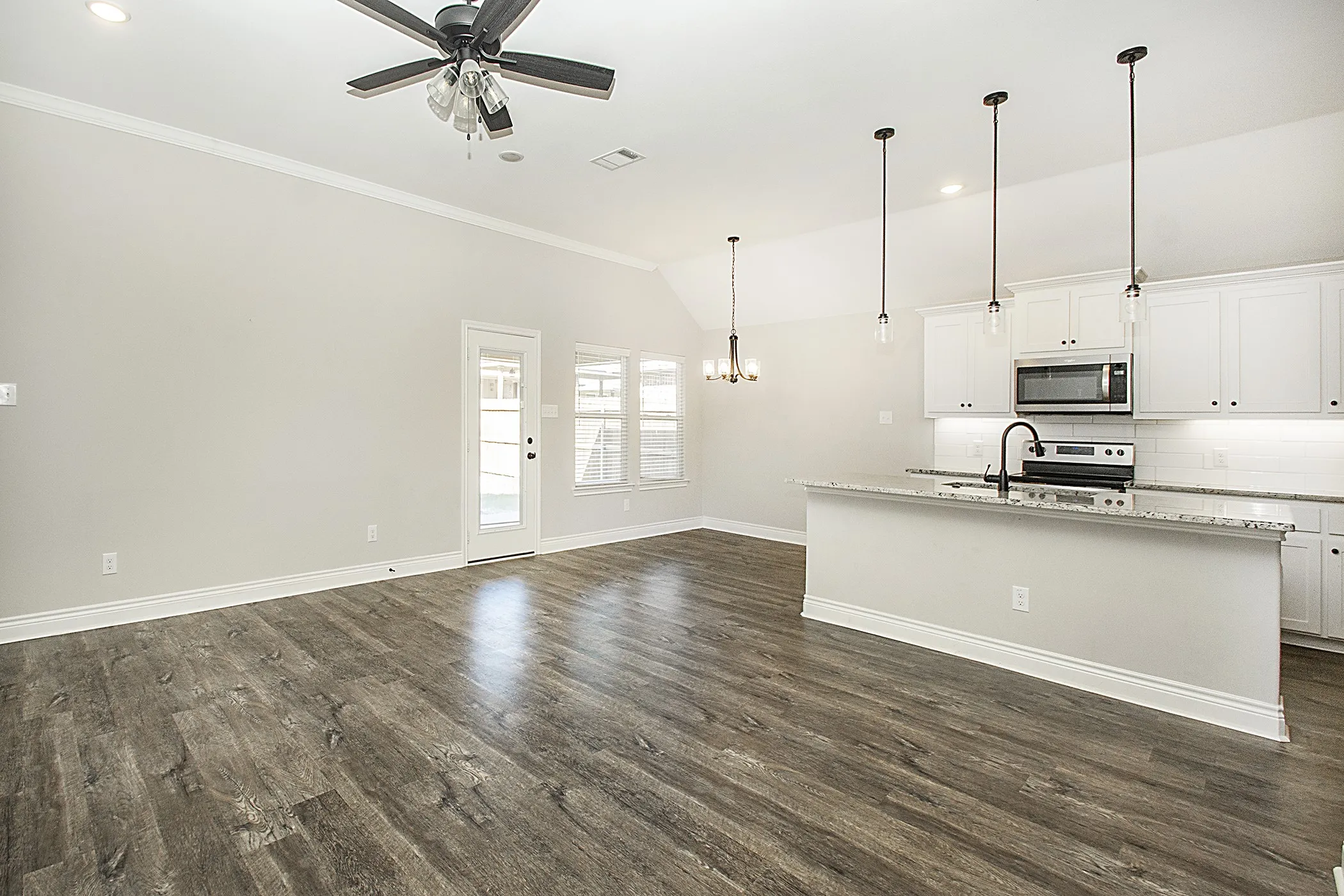 Vaulted ceilings with a ceiling fan, wood-finish flooring, white kitchen cabinetry, granite countertops, and stainless steel appliances