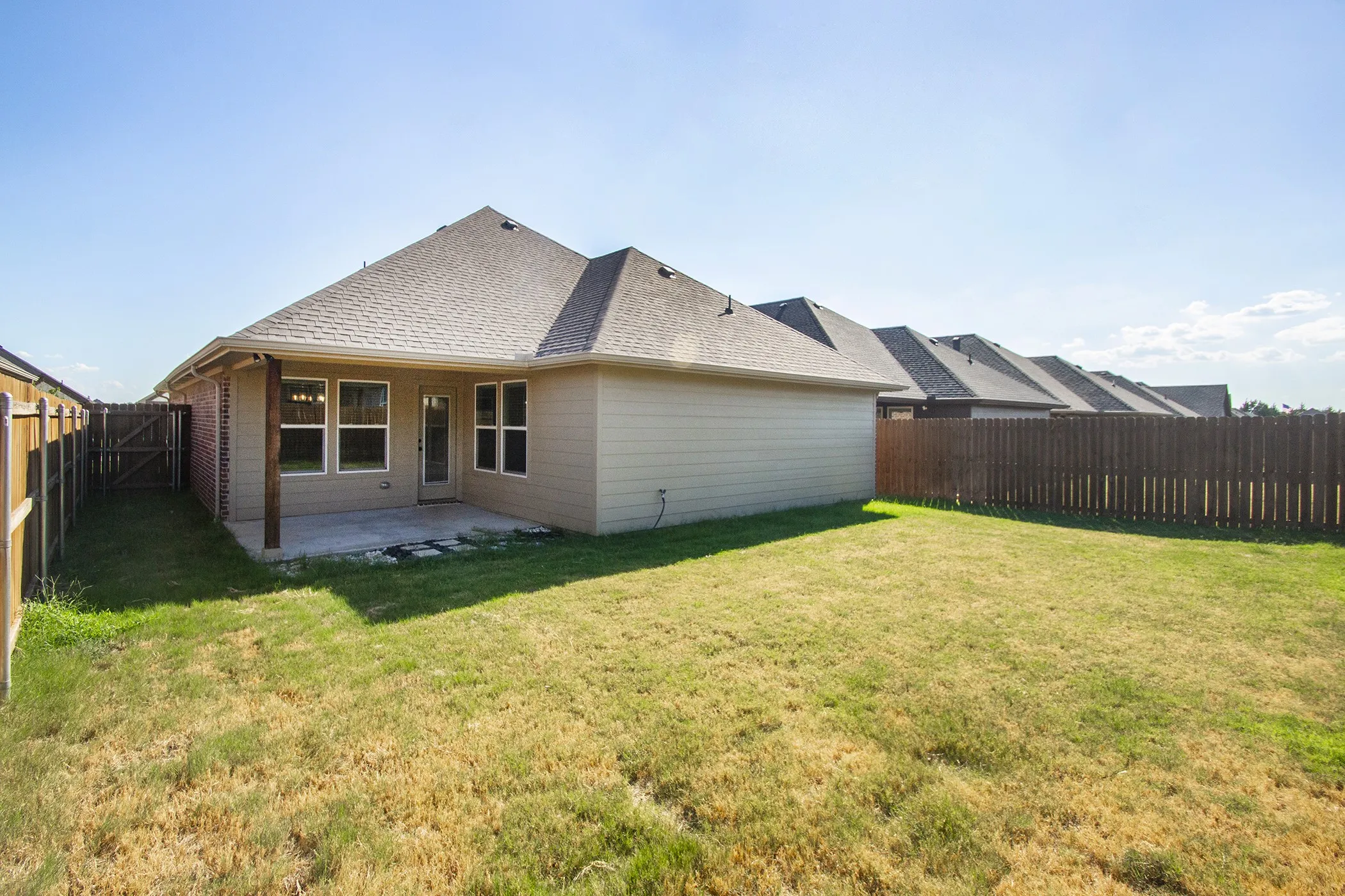 Expansive backyard featuring a covered concrete patio, multiple windows, and a privacy fence