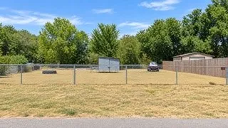 Spacious fenced lot with mature tree-lined perimeter, gravel and cleared grounds, detached storage structures, and direct driveway access