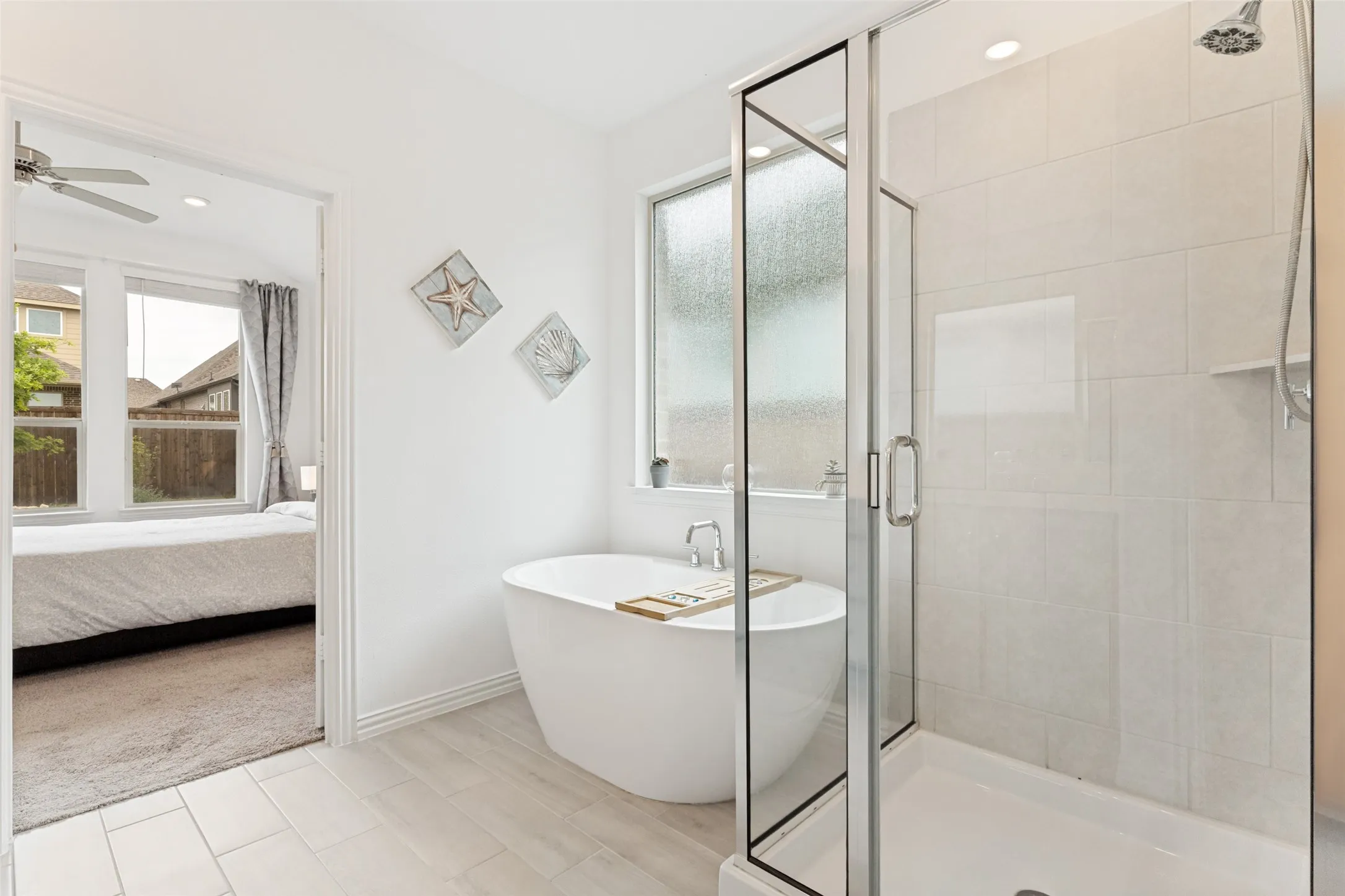 Freestanding soaking tub, glass-enclosed shower with tiled walls, natural light from privacy glass window, recessed ceiling lighting, and wood-look tile flooring