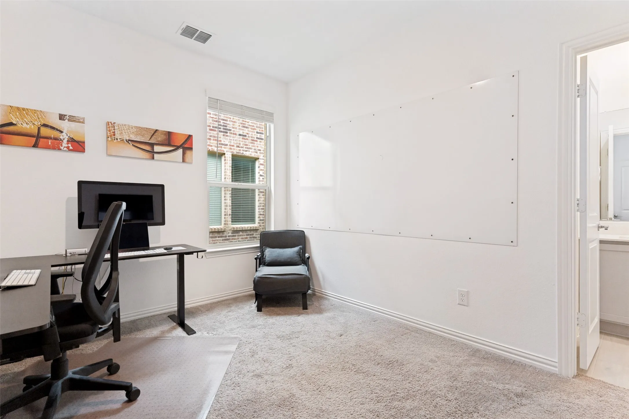 Carpeted room with a fixed wall-mounted whiteboard and a window featuring brick exterior