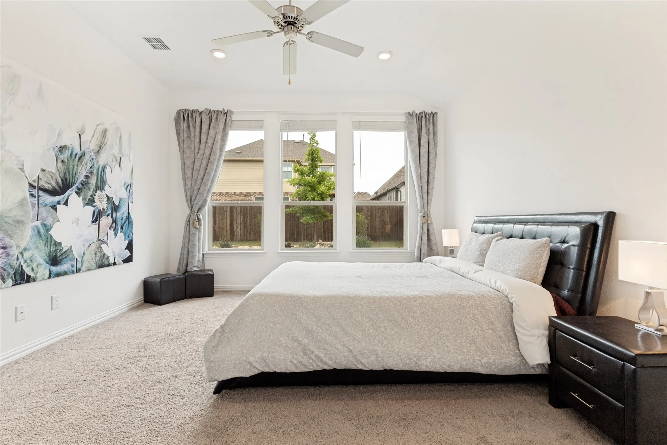 Expansive room featuring light-toned carpet flooring, three large windows, a ceiling fan with integrated lighting, and recessed ceiling lights
