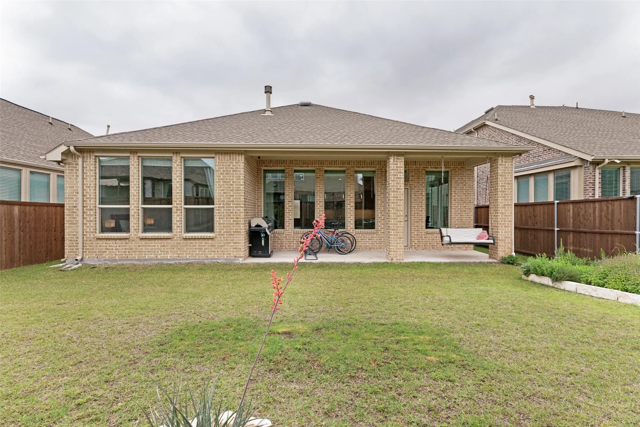 Spacious backyard with a covered patio, brick exterior, multiple windows, and a privacy fence