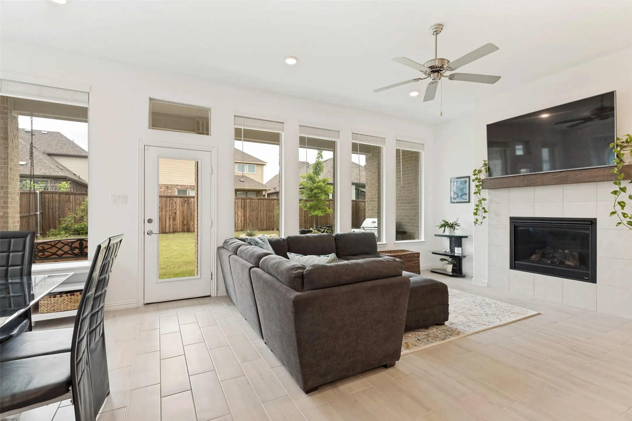 Open-concept living space featuring wood-finish flooring, a tiled fireplace with wood mantel, multiple windows, and a ceiling fan