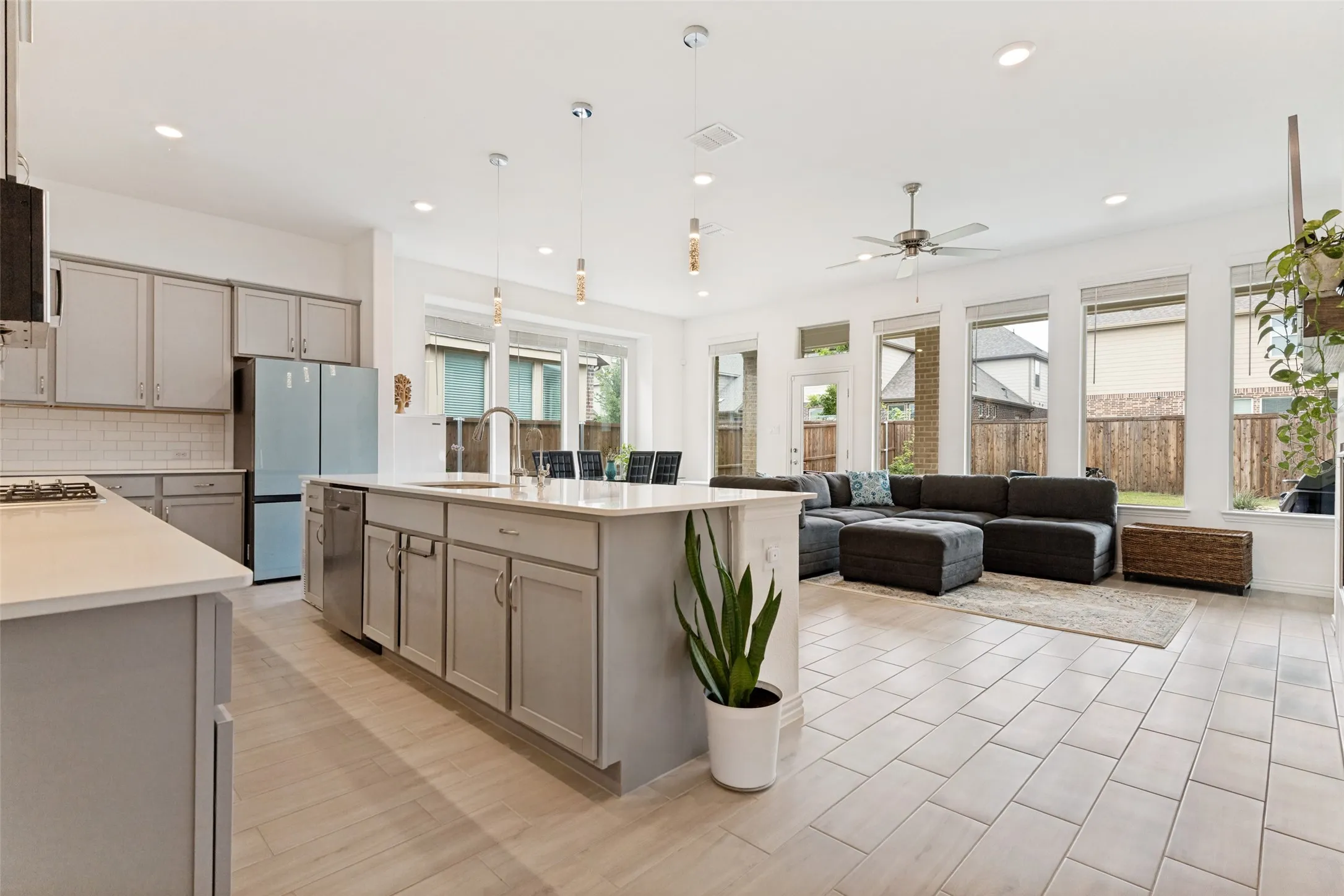 Open-concept living space with tile flooring, a kitchen island with a sink, white countertops, and a full wall of windows