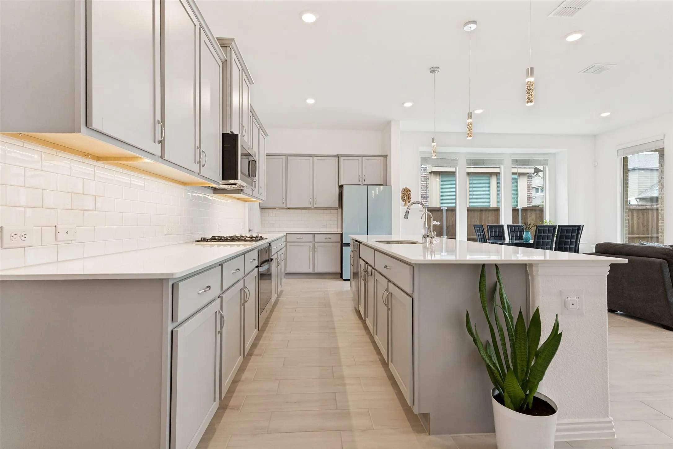 Spacious kitchen featuring an expansive center island with an integrated sink, light-toned cabinetry, white subway tile backsplash, and recessed lighting