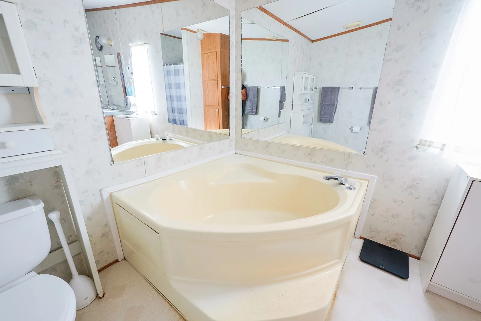 Corner soaking tub with deck-mounted faucet and surrounding mirrors, complemented by a built-in toilet and integrated storage cabinetry