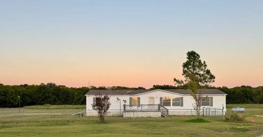 White exterior with a front deck and mature trees