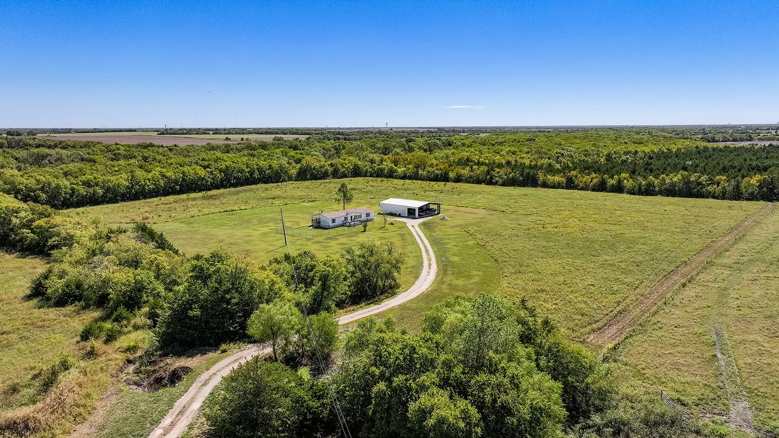 Expansive acreage featuring a single-story residence, a large outbuilding, and a winding driveway