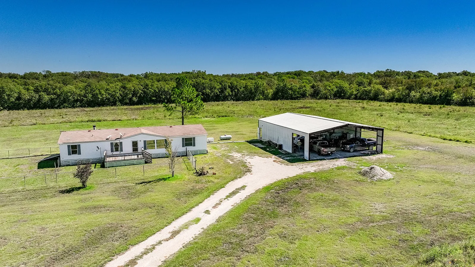 Expansive green acreage with a single-story residence, a large detached metal structure, and a gravel drive