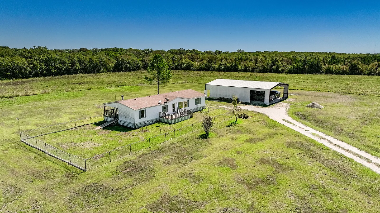 Expansive green acreage with a single-story residence, detached covered structure, and a dedicated driveway