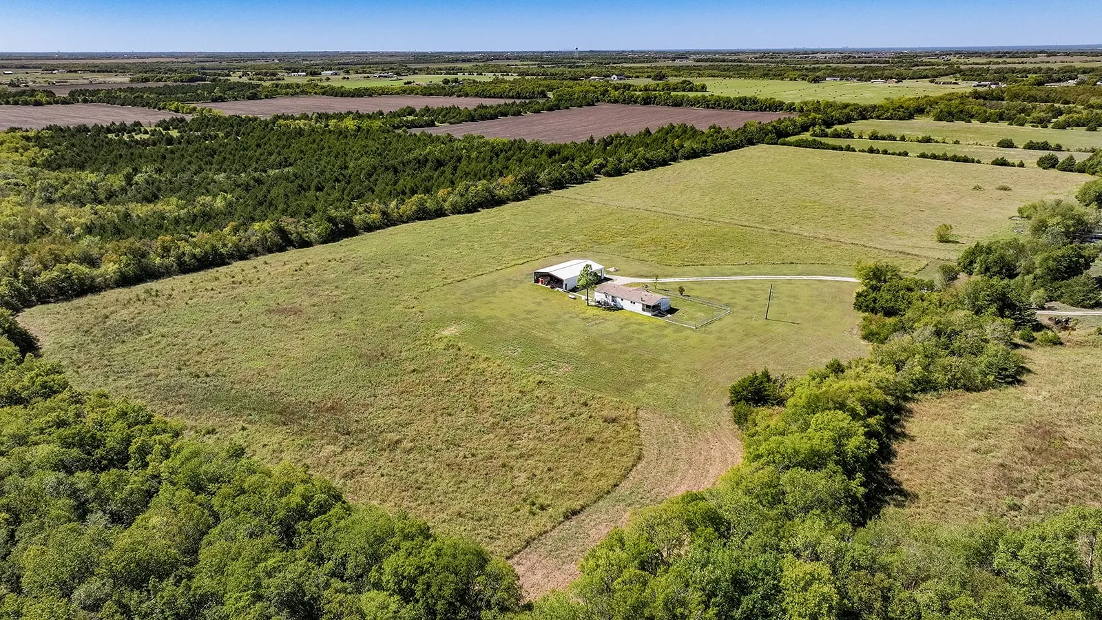 Expansive land parcel featuring open fields, wooded borders, a residential structure, and an additional outbuilding
