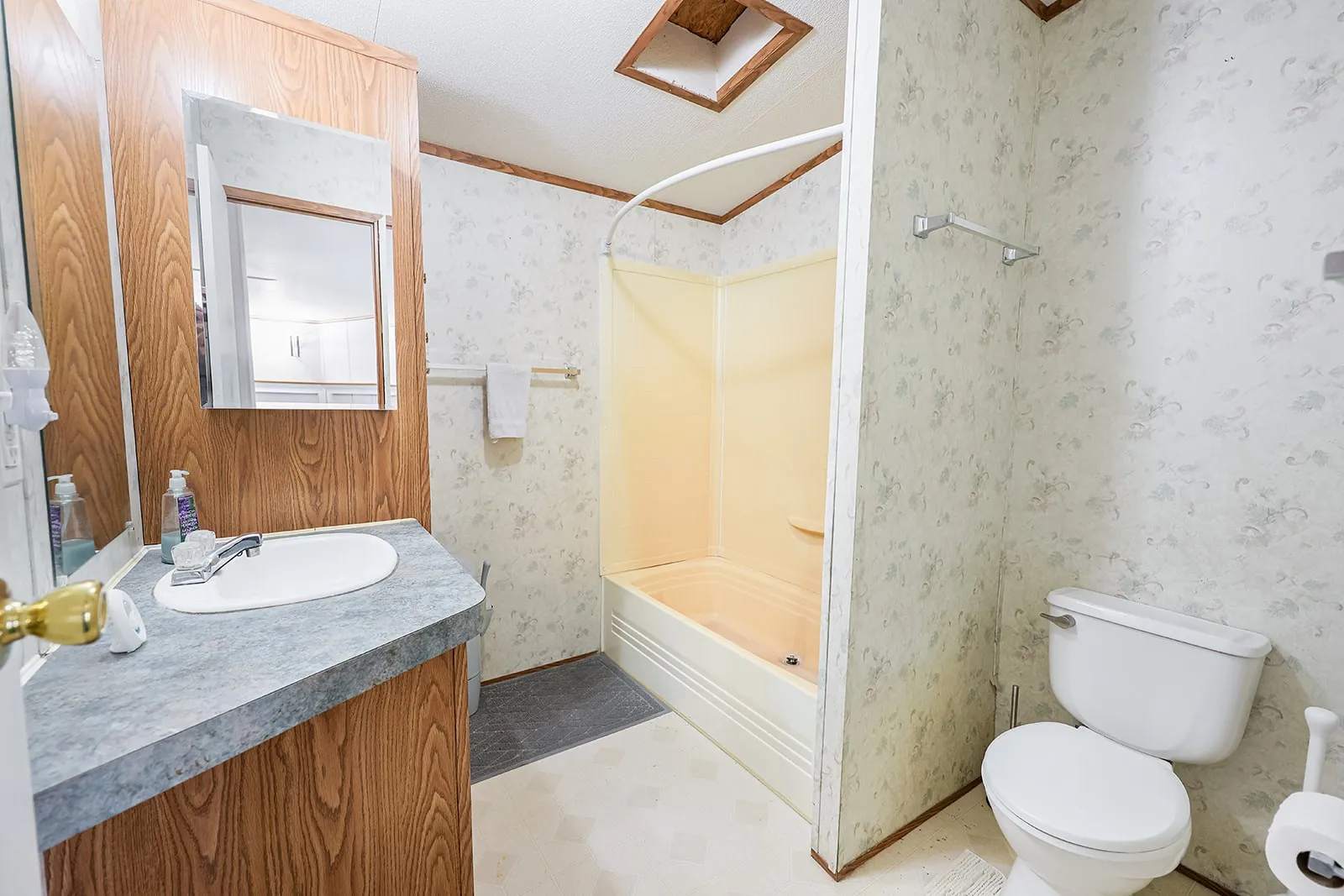 Bathroom featuring a wood-finish vanity with a gray countertop, a built-in tub/shower combination, and a white toilet