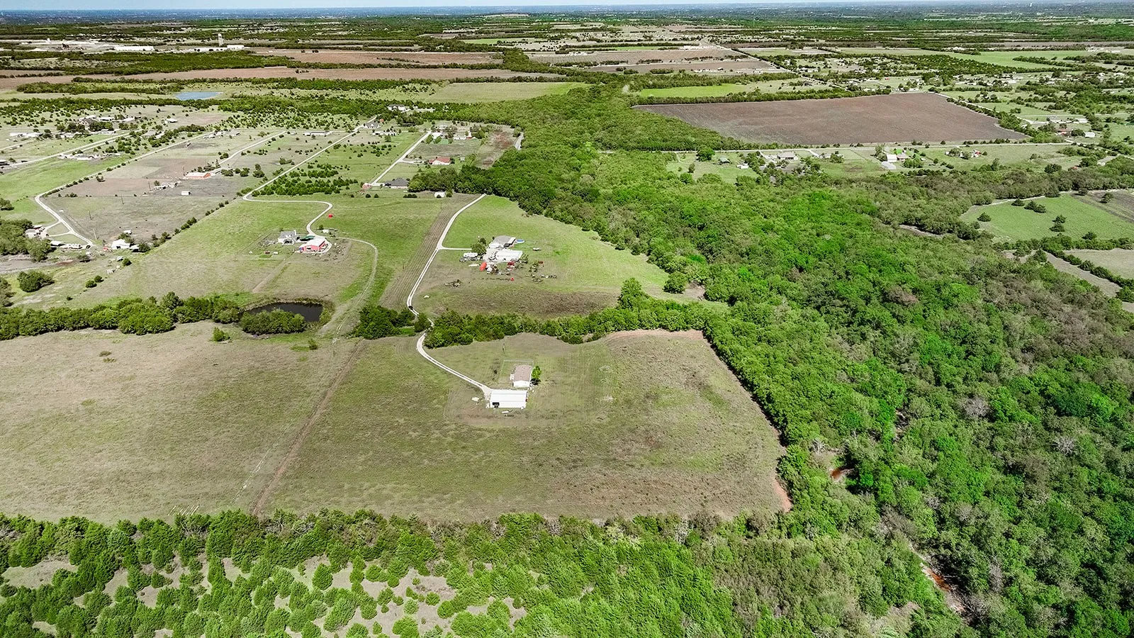 Expansive land featuring a natural pond, lush green tree lines, and a developed parcel with a residential structure