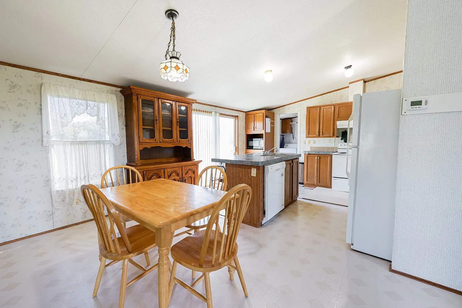 Open-concept kitchen and dining area featuring wood-finish cabinetry, a central island with an integrated sink, and white appliances