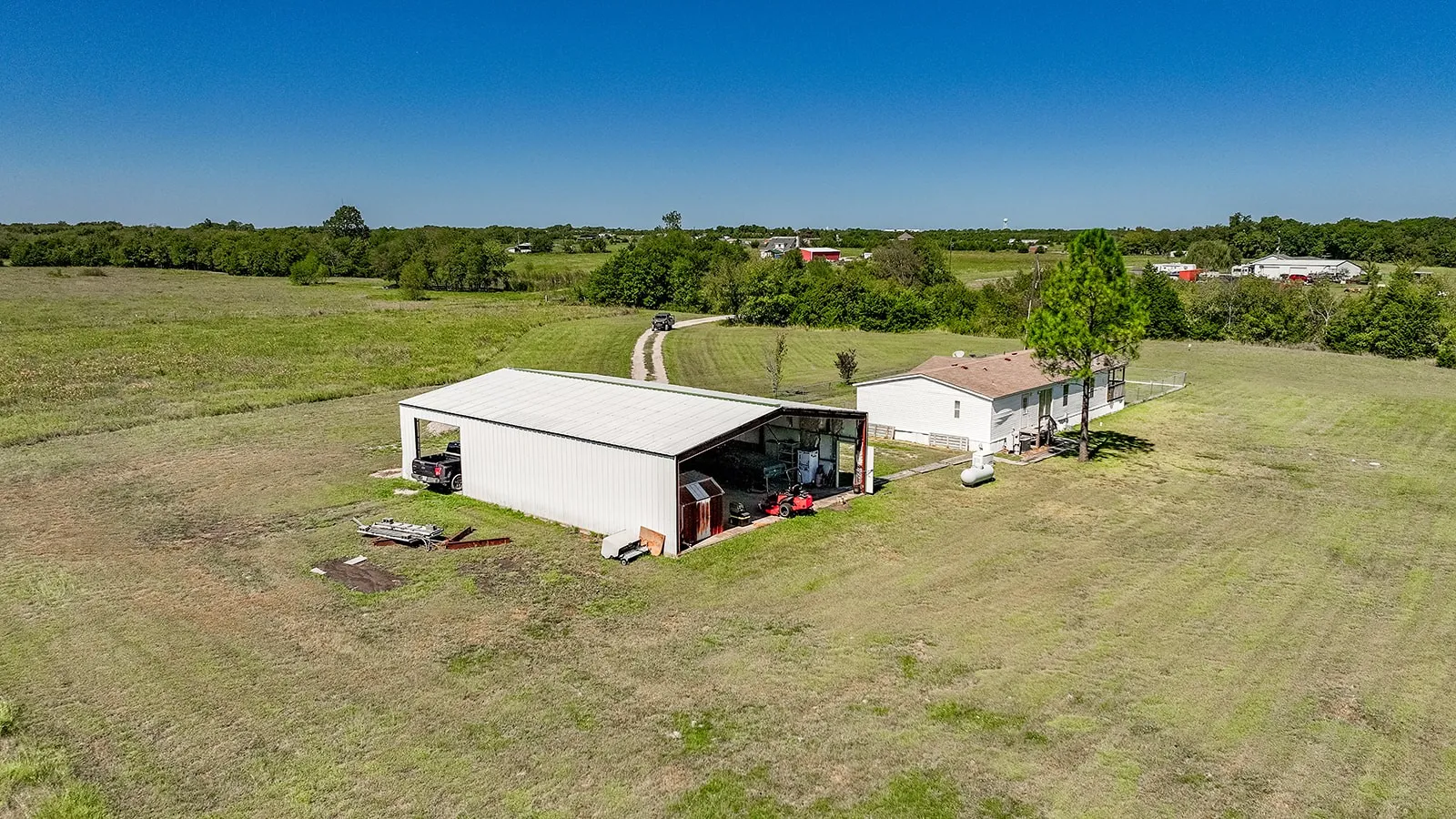 Expansive grassy lot featuring a single-story residence and a large metal outbuilding with open bays