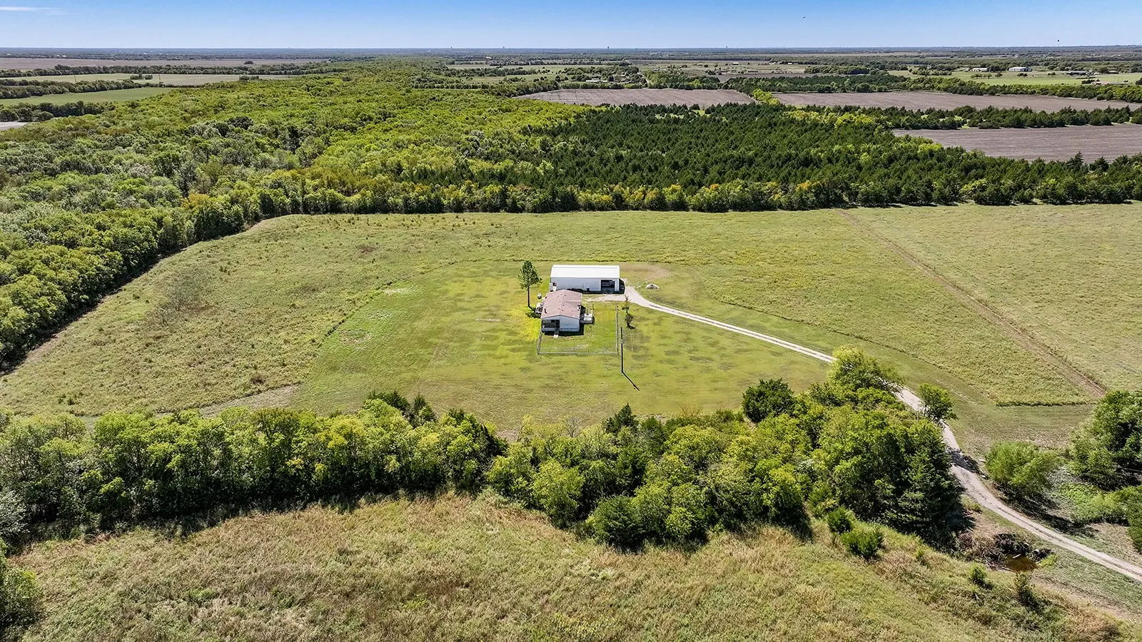 Expansive property featuring a single-story residence with an attached garage, a detached ancillary building, a winding driveway, and surrounding natural landscapes