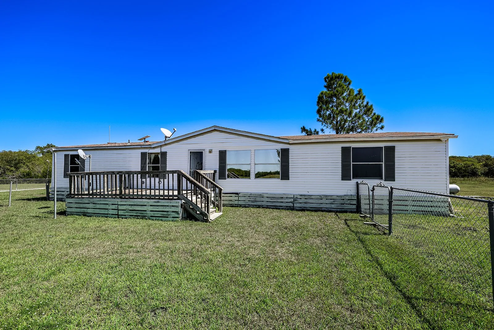 White horizontal siding exterior with dark shutters, front wooden deck, and a chain-link fence