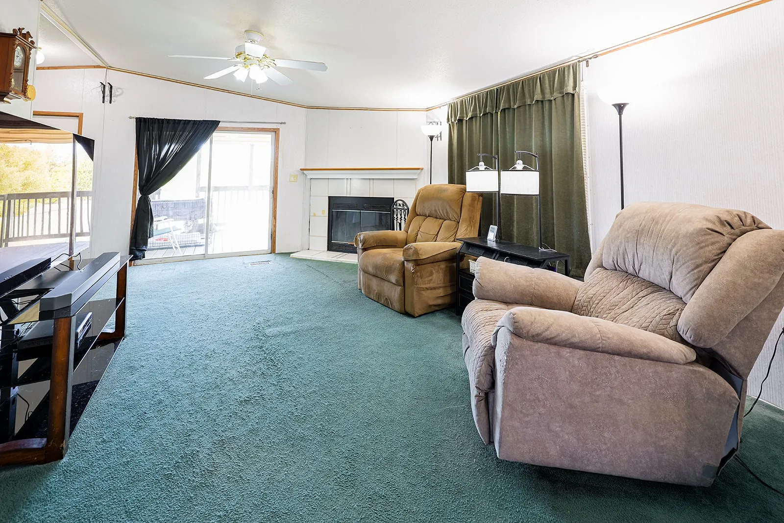Fireplace with white mantel, ceiling fan, sliding glass door, and green carpeting