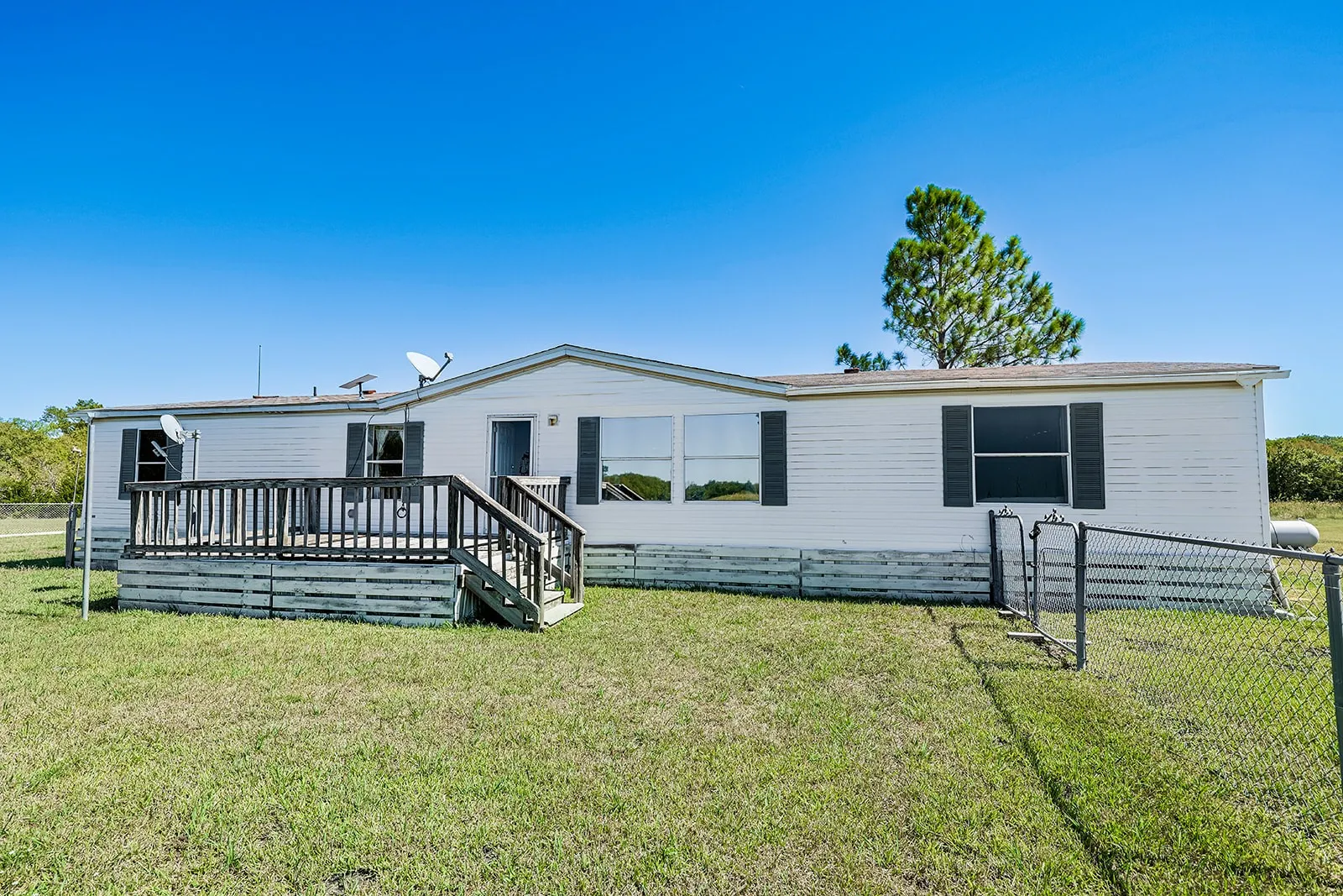 Exterior featuring white siding, a built-in wooden deck with railings, dark window shutters, and a chain-link fence