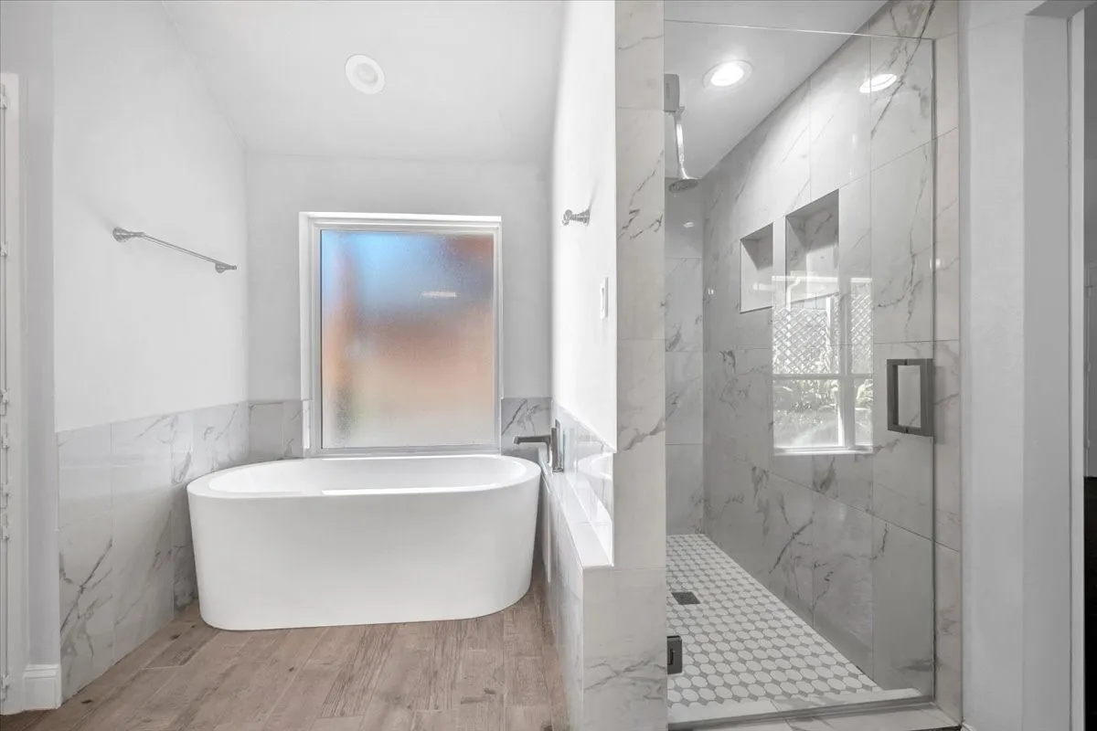 Freestanding soaking tub with a frosted window, glass-enclosed shower, wall-mounted shower niches