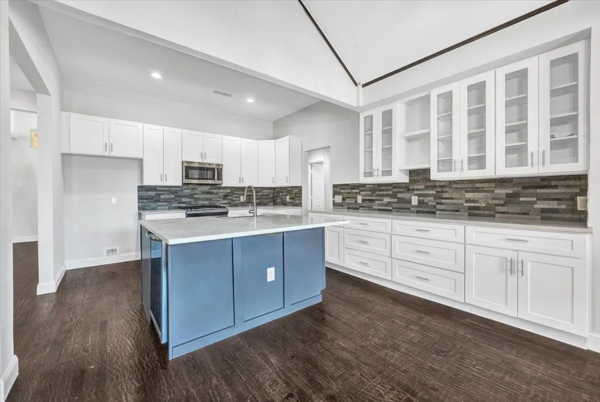Kitchen featuring a central island, countertop, stainless steel appliances, extensive white cabinetry with glass-front uppers, and built-in wine fridge