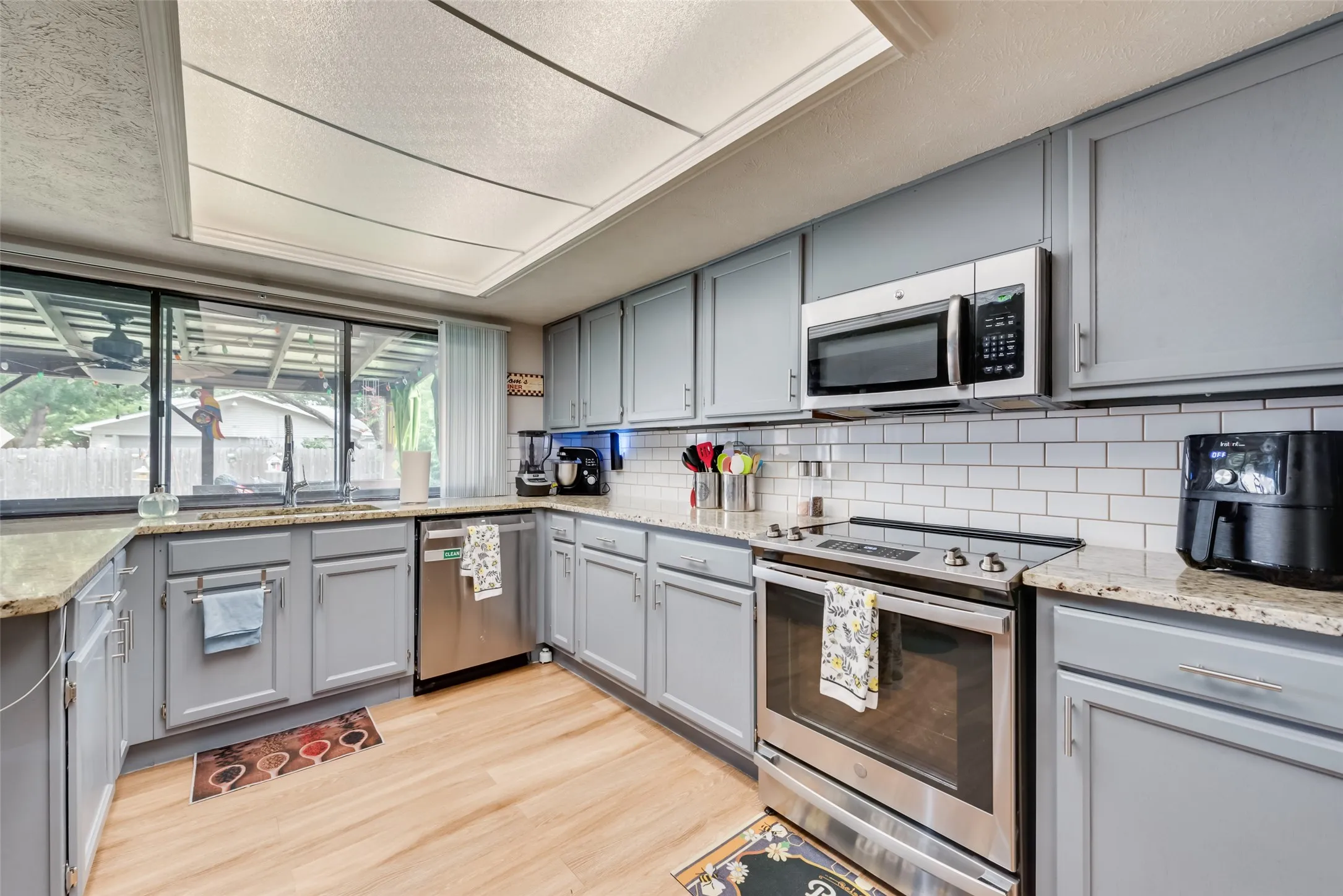 Kitchen featuring gray cabinetry, stainless steel appliances, light stone counters, decorative backsplash, and light wood finished floors
