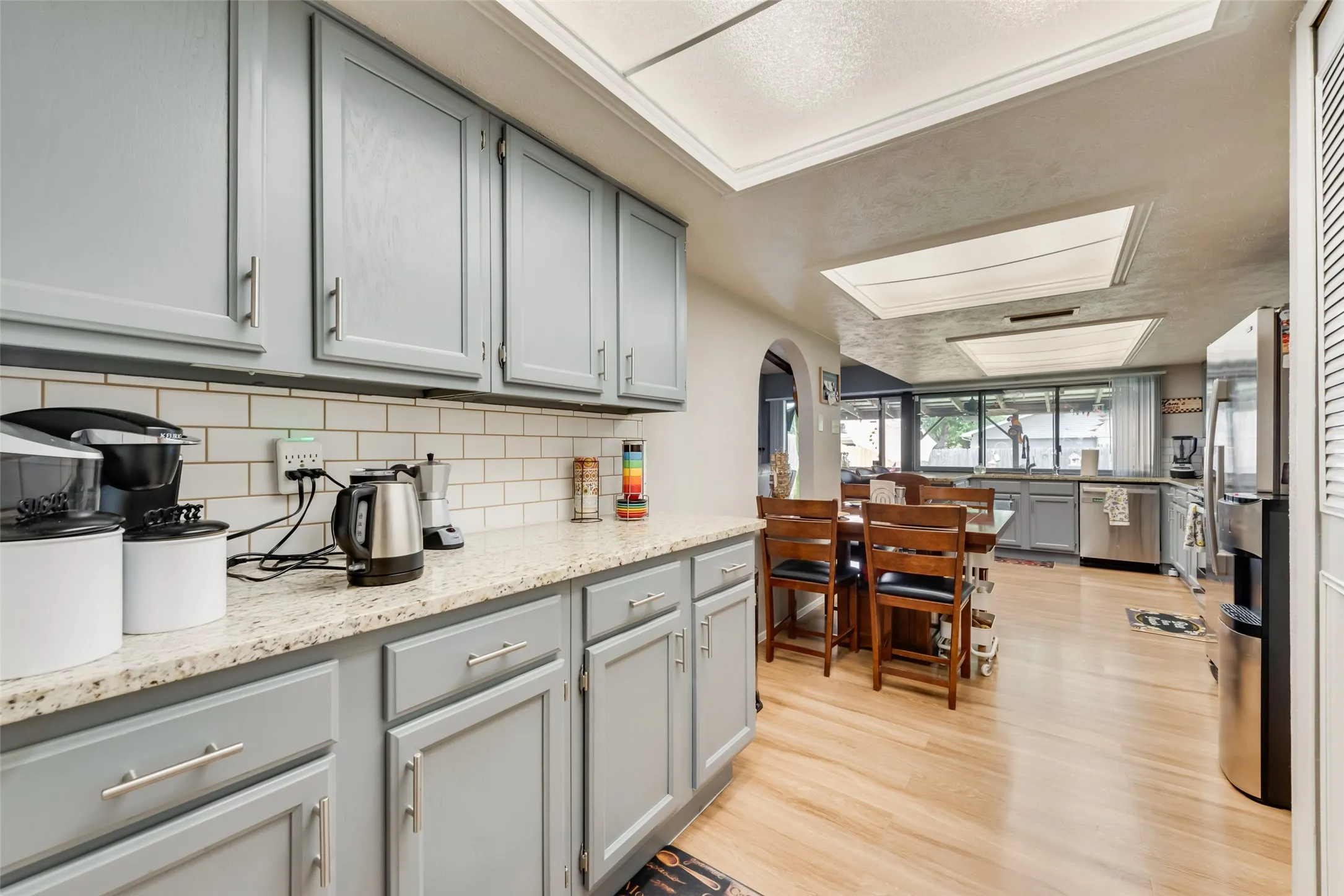 Kitchen with gray cabinets, light wood-type flooring, stainless steel appliances, light stone counters, and arched walkways