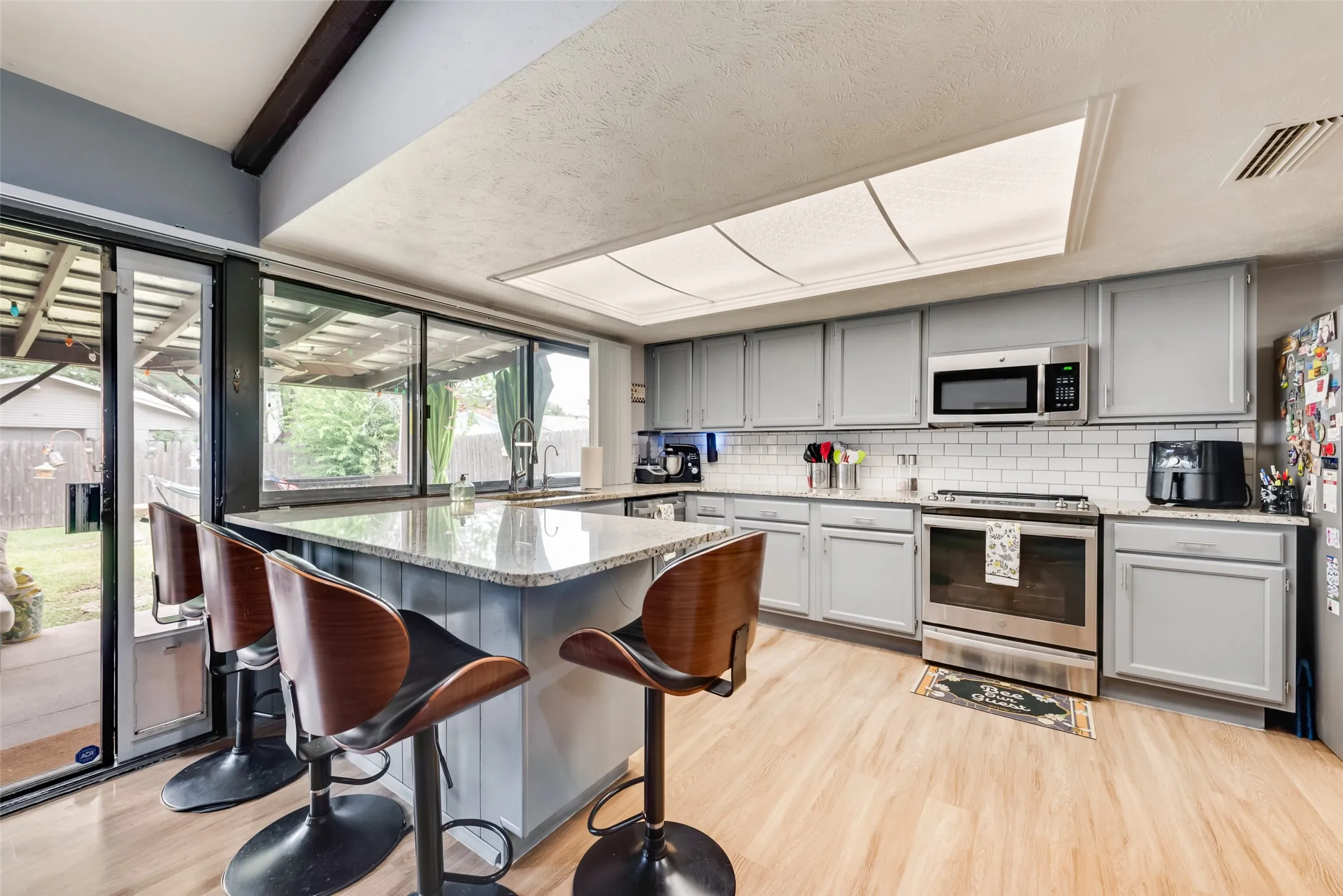 Kitchen featuring gray cabinets, appliances with stainless steel finishes, decorative backsplash, and a peninsula