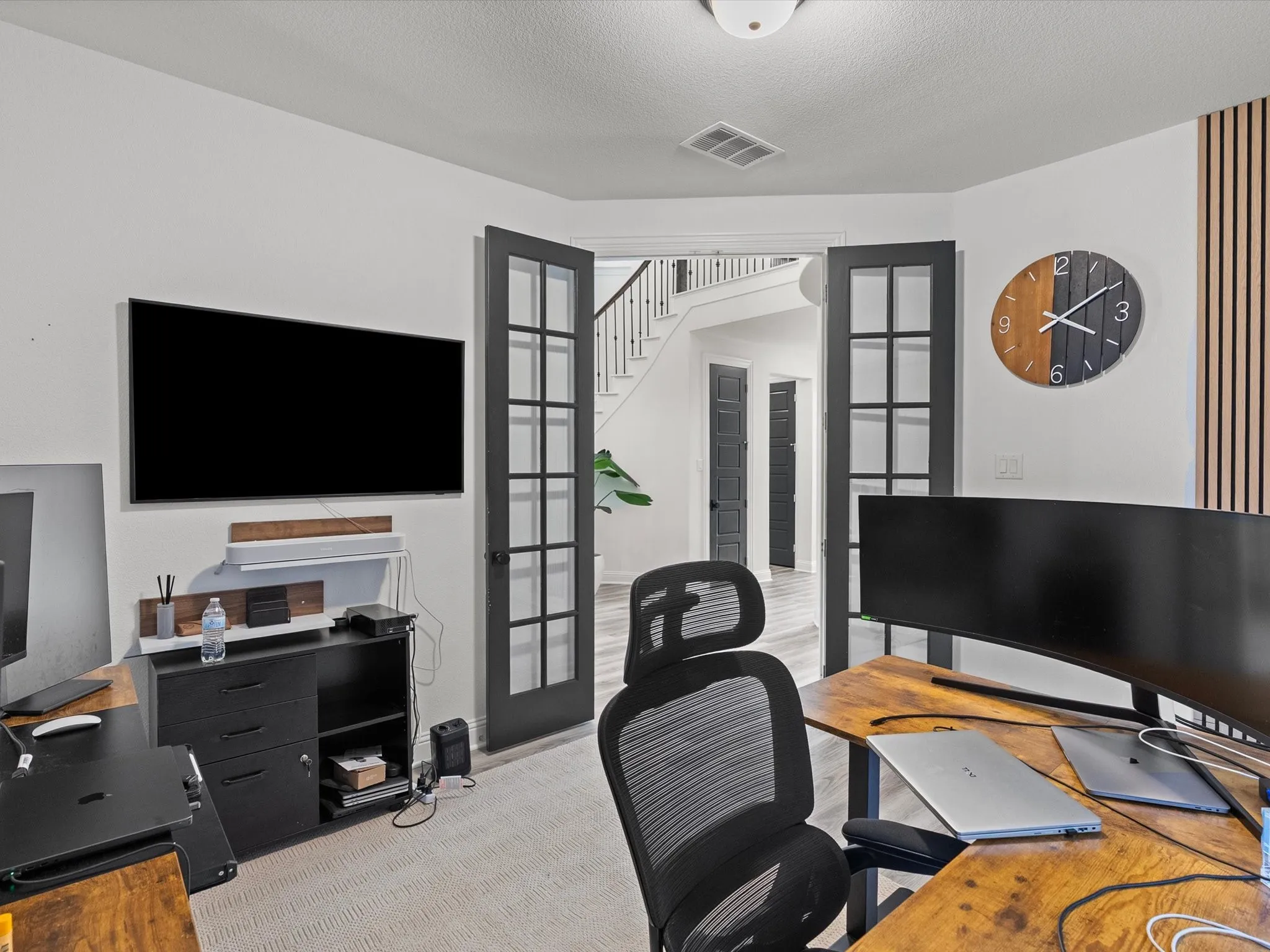 Double French doors, light wood-finish flooring, white walls, recessed lighting, and a white staircase with dark railings