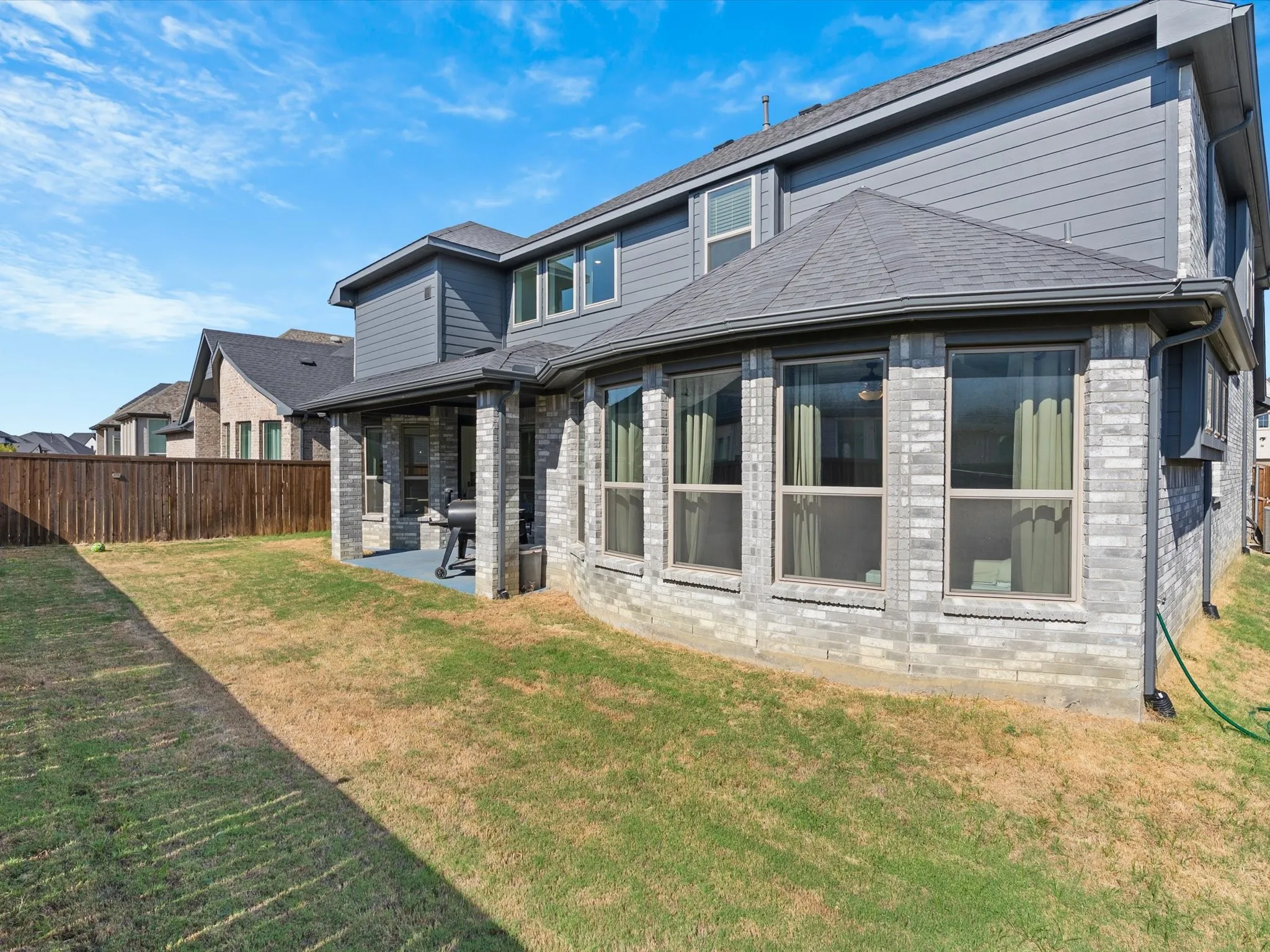 Exterior featuring durable brick and siding construction, covered patio, multiple windows, and a fenced backyard