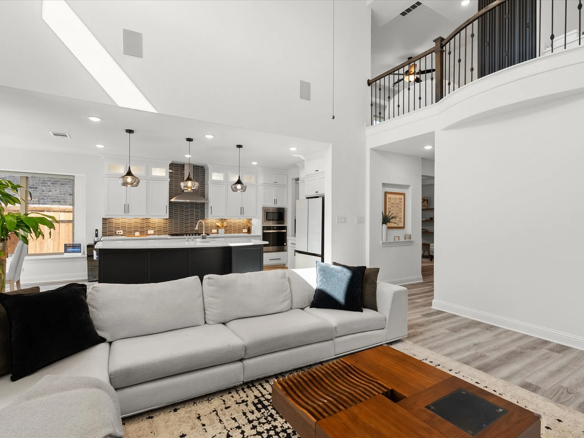 Vaulted ceiling with skylight, open-concept kitchen with island, wood-finish flooring, and a second-story balcony with metal balusters