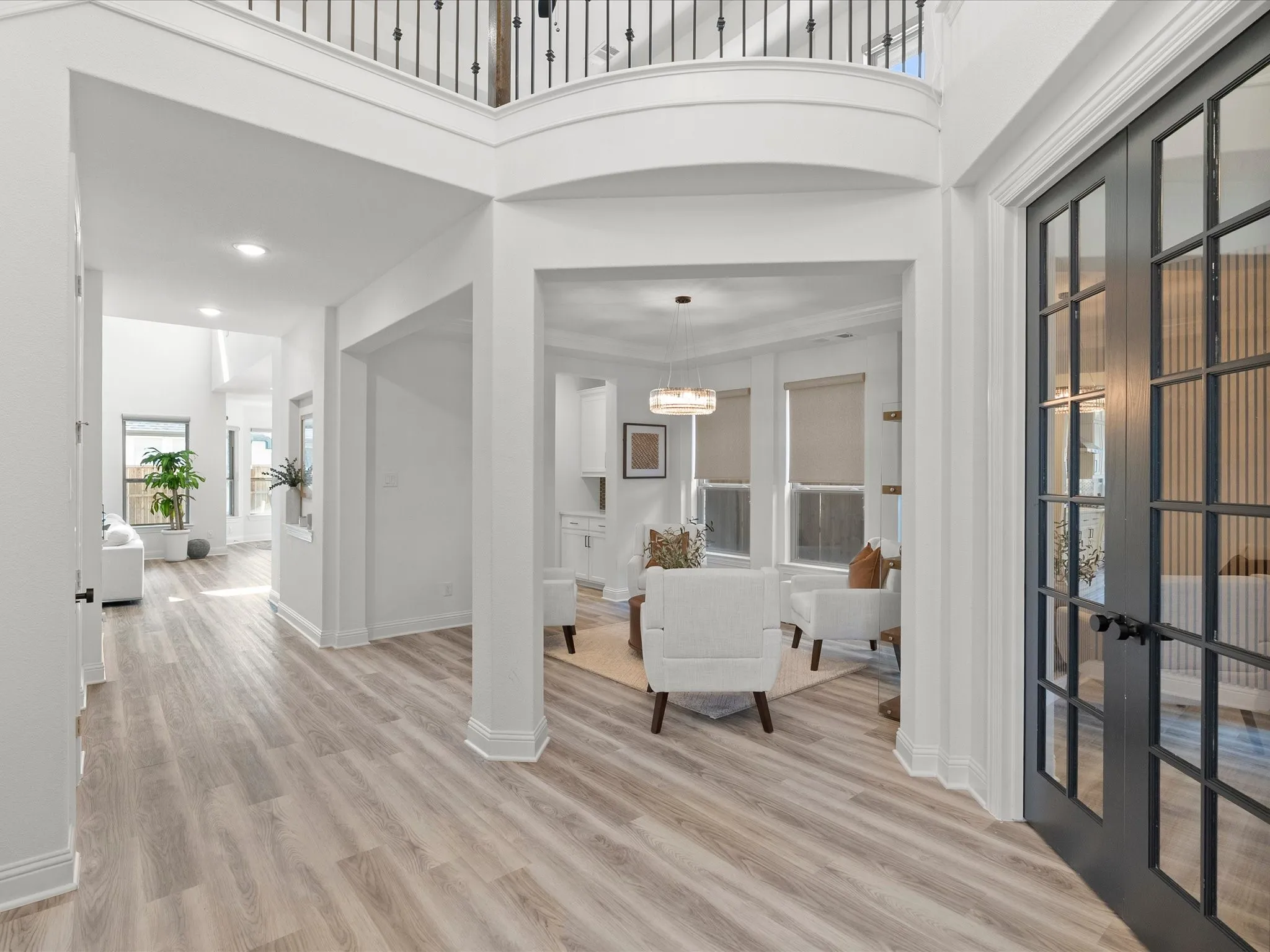 Spacious entry with wood-finish flooring, two-story ceiling, and dark-framed glass paneled double doors