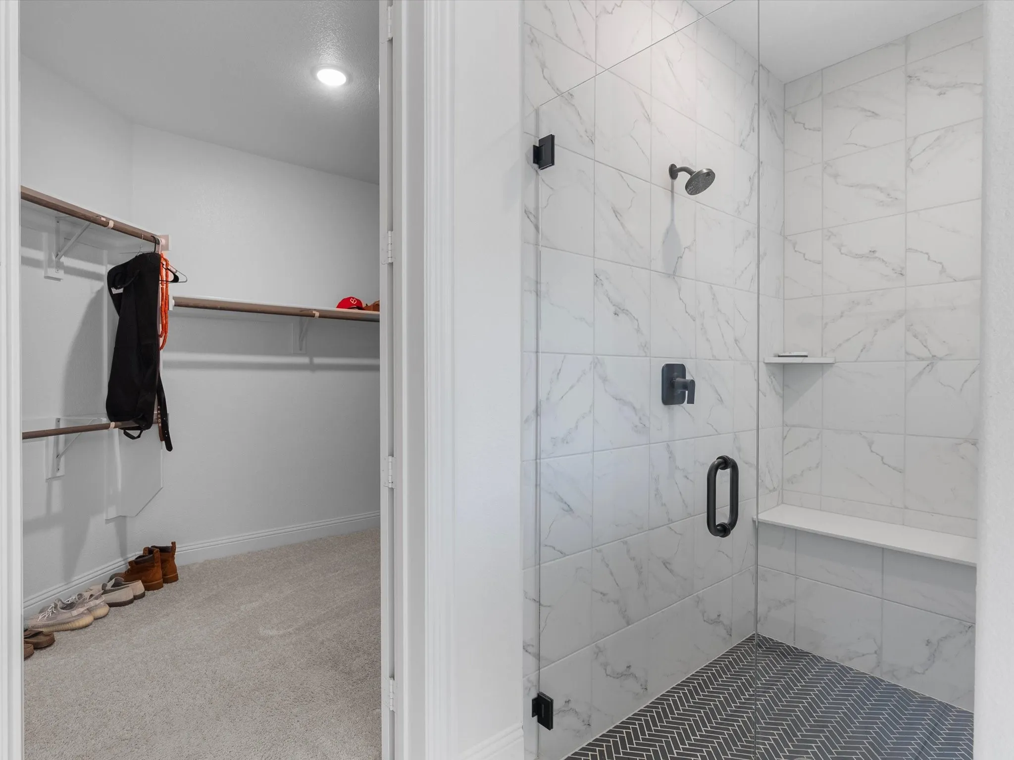 Walk-in closet with built-in shelving, shower with herringbone tile flooring, large-format wall tile, built-in shower bench, and matte black fixtures